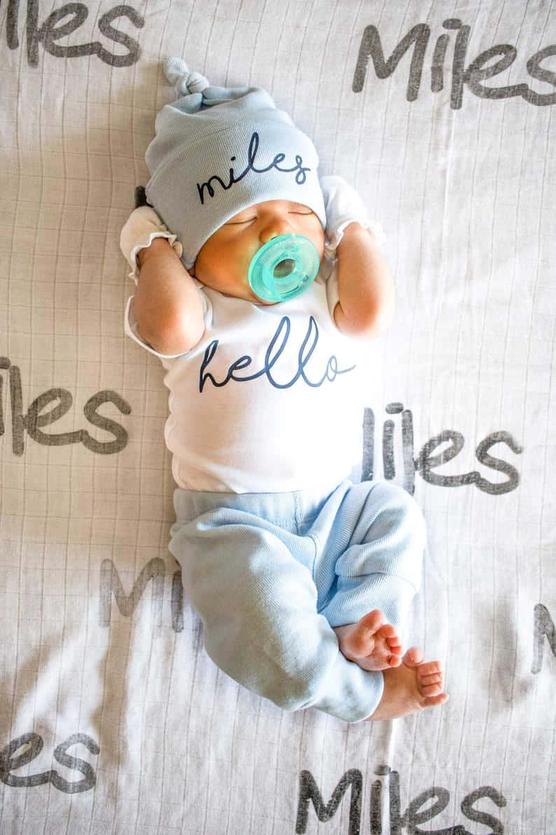 Boy 桌布 壁紙 — 一個名叫Miles的熟睡新生嬰兒，戴著印有他名字和「你好」字樣的配套帽子和襯衫，躺在圖案毯子上休息。