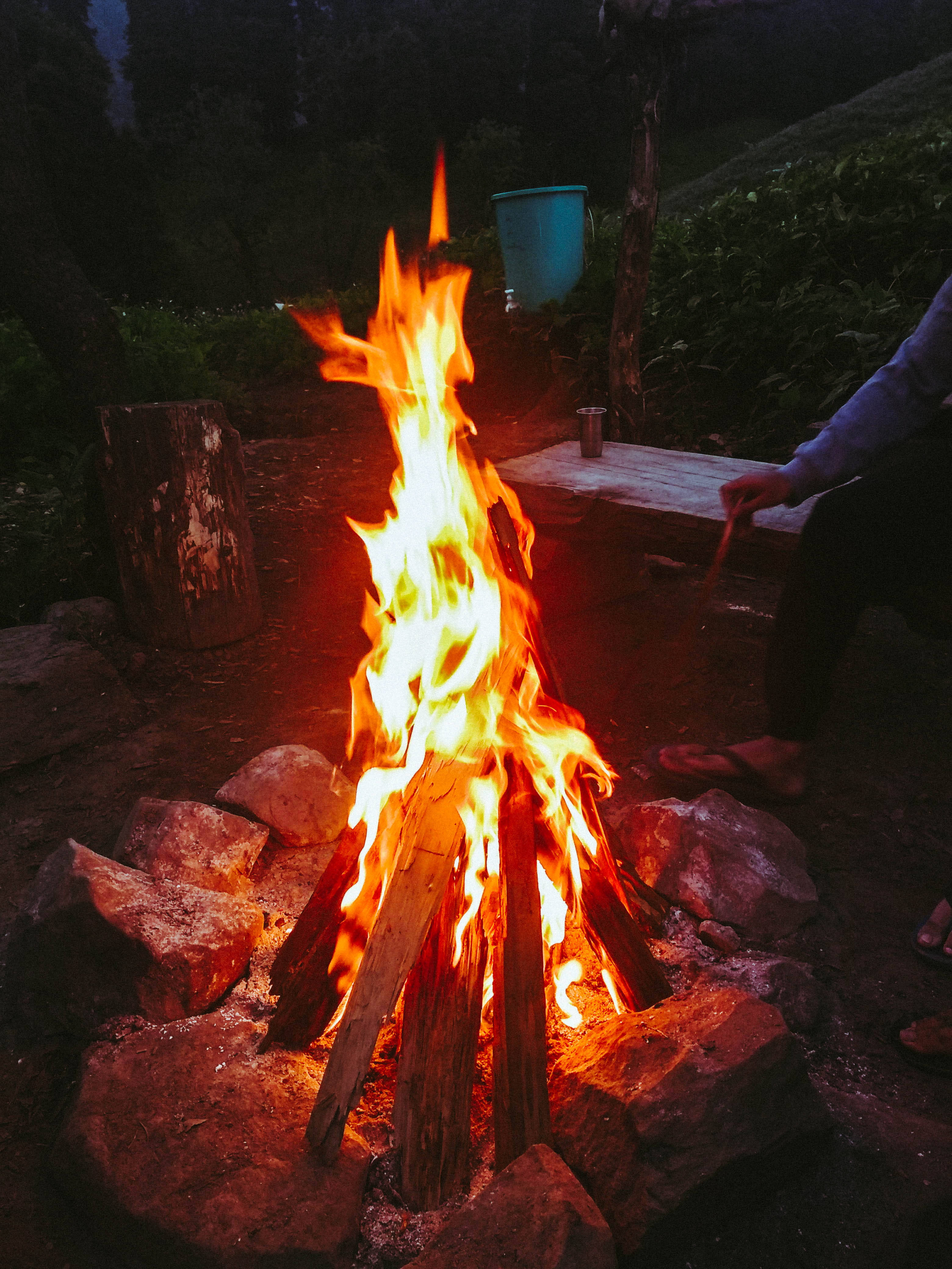 火焰動畫 桌布 壁紙 — 一個咆哮的營火在石環中劈啪作響，夜空下，附近有人在照料火焰。