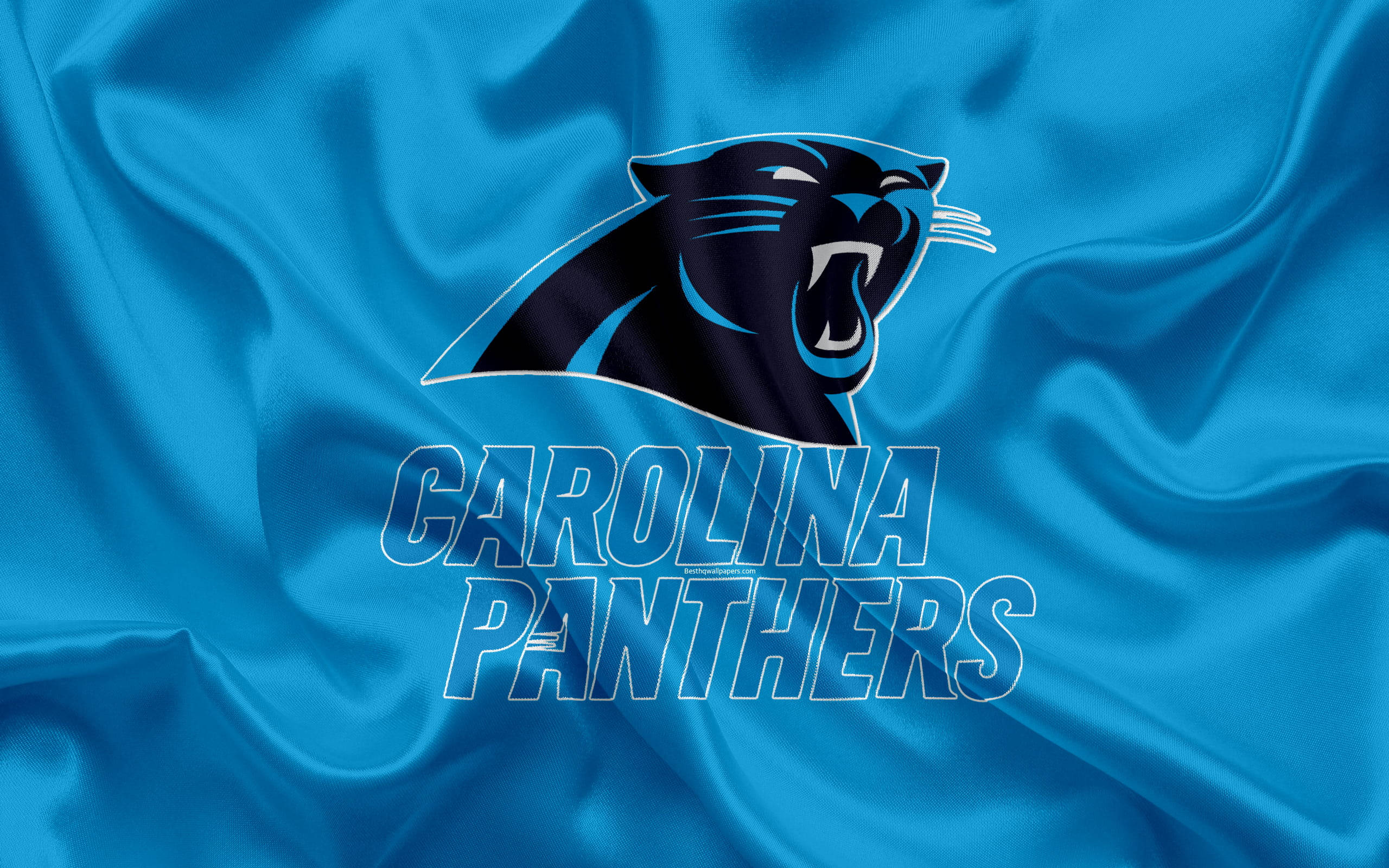 淺藍色 桌布 壁紙 — 一個咆哮的黑豹標誌，上面有「CAROLINA PANTHERS」文字，背景是流動的皇家藍色緞面布料。