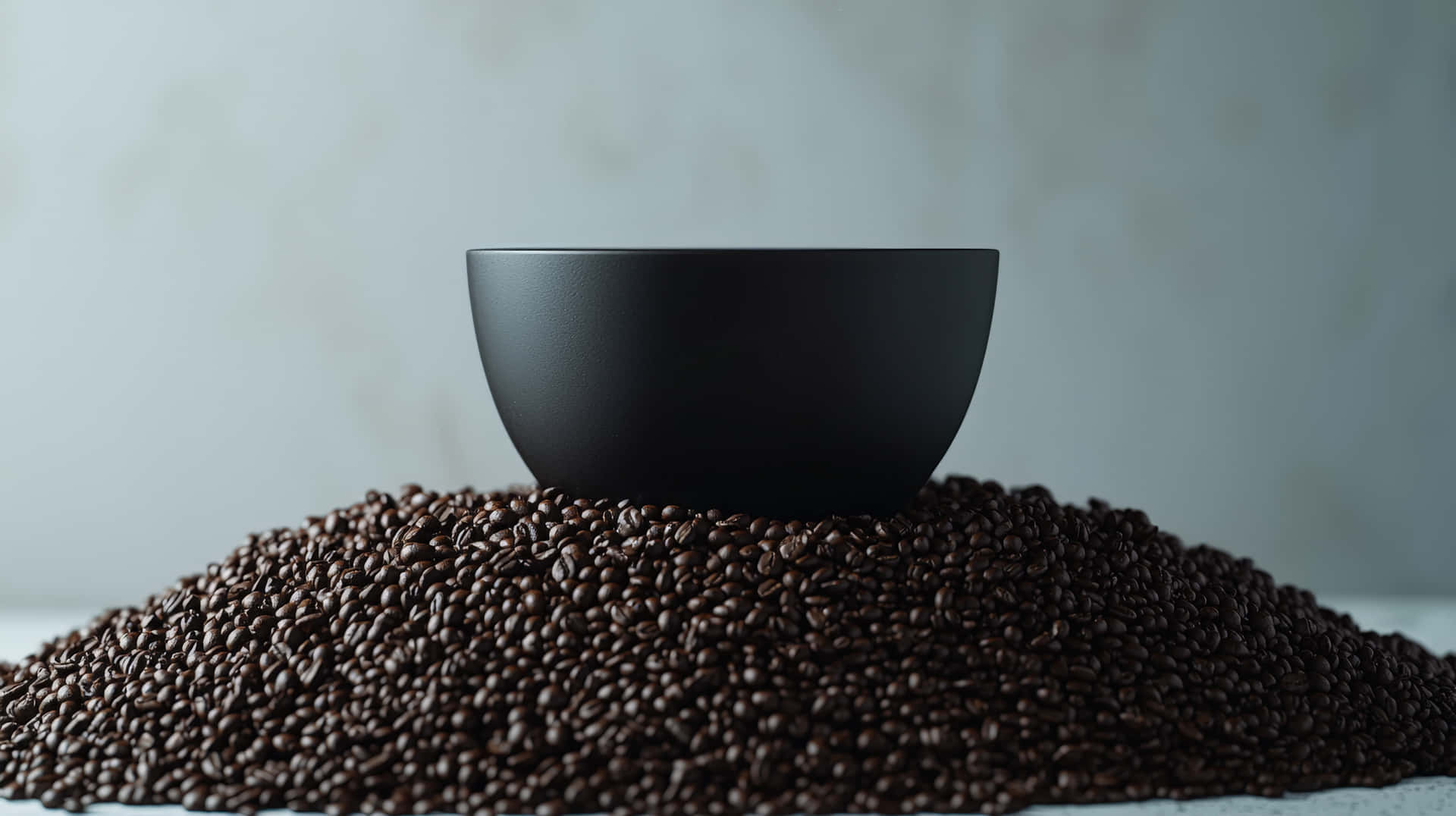 Black Bowl on Pile of Coffee Beans 壁紙 — 一個啞光黑色碗居中放置在深烘焙咖啡豆堆上，背景為柔和的灰色。