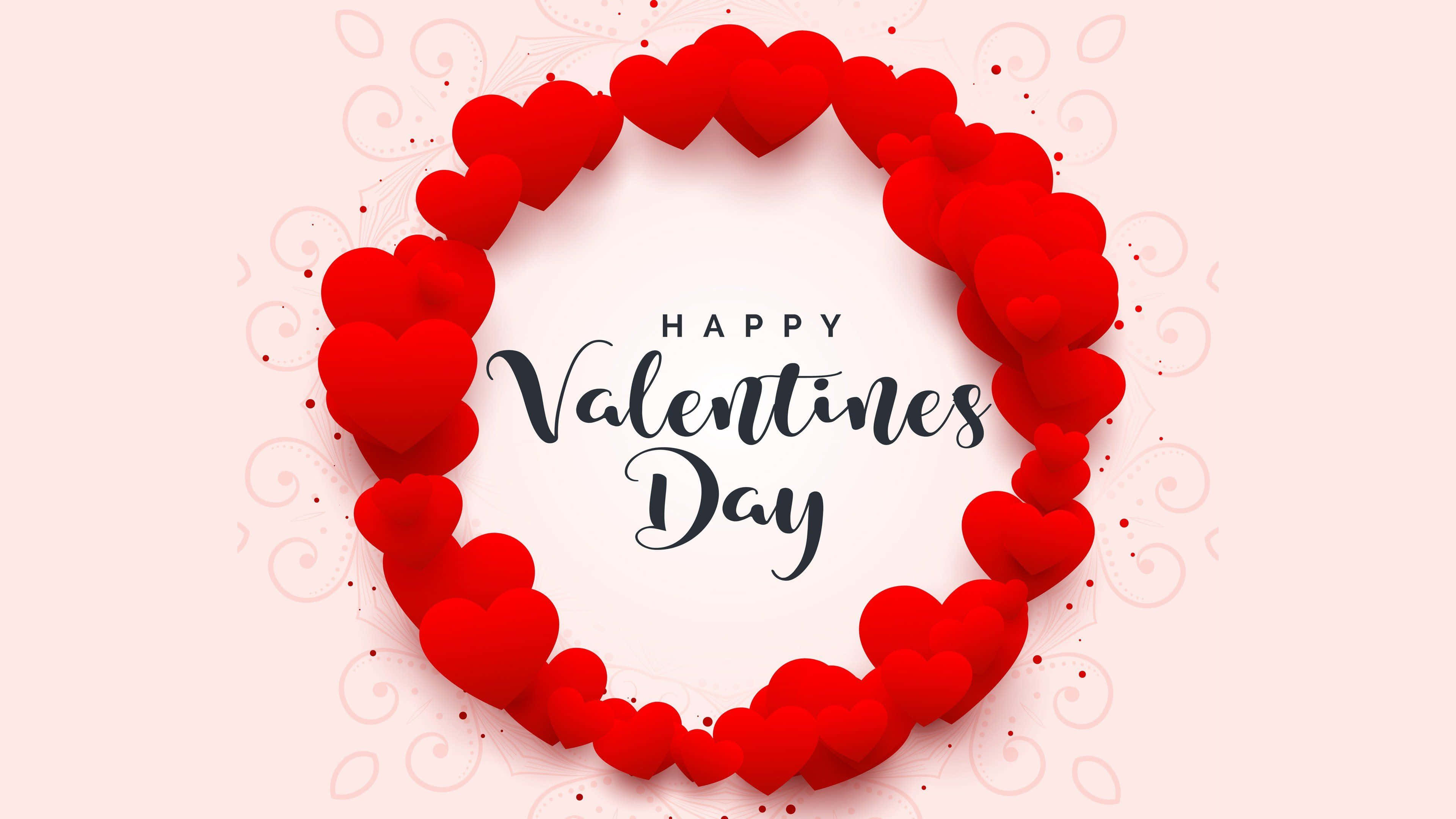 Valentines 桌布 壁紙 — 一個喜慶的情人節祝福，由層疊的紅色心形組成的圓形花環框在柔和的粉紅色背景上。