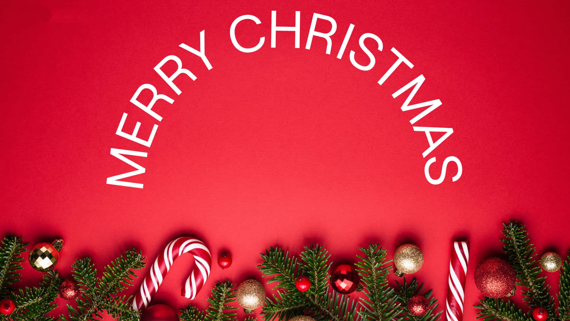  壁紙 — 一個喜慶的紅色背景，上面有白色文字 'MERRY CHRISTMAS' 拱形排列在松樹枝、拐杖糖和裝飾品的邊框上方。