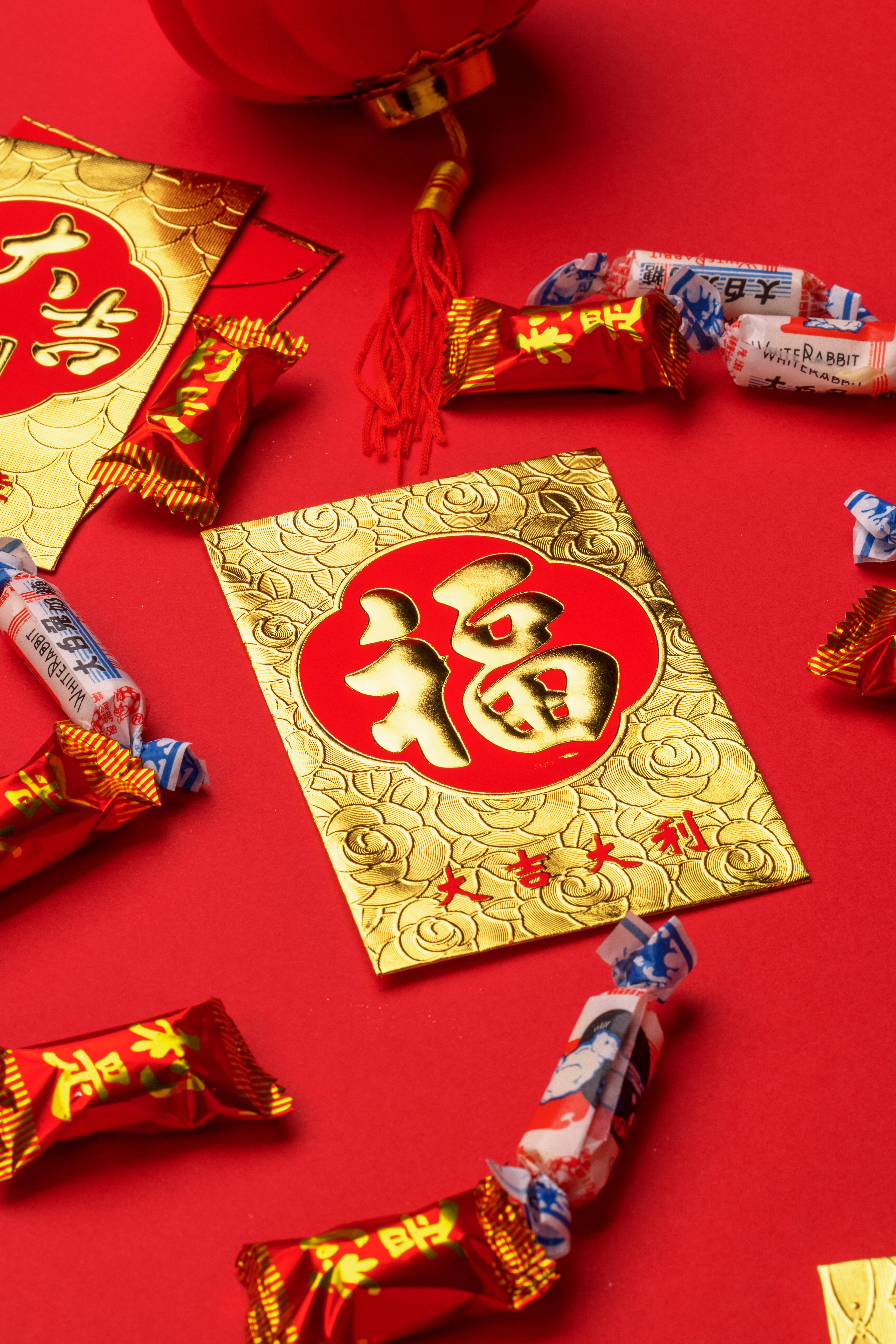 春節 桌布 壁紙 — 一個喜慶的紅色背景，飾有金色紅包，上面有「福」字，周圍散落著紅色和藍色包裝的糖果。