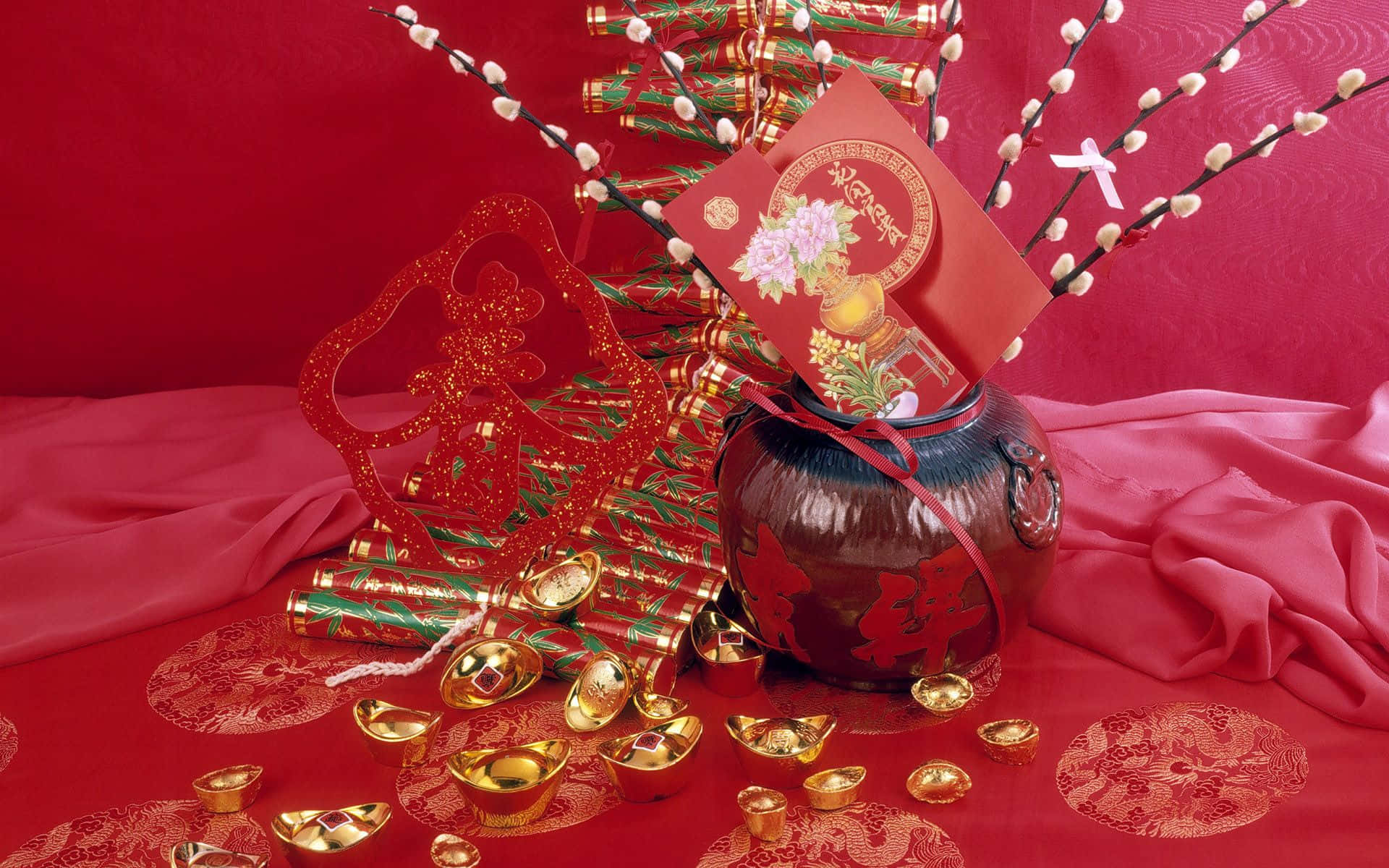 春節 桌布 壁紙 — 一個喜慶的紅金色中國新年佈置，在豐富的紅色布料背景上擺放著裝飾品和金元寶。