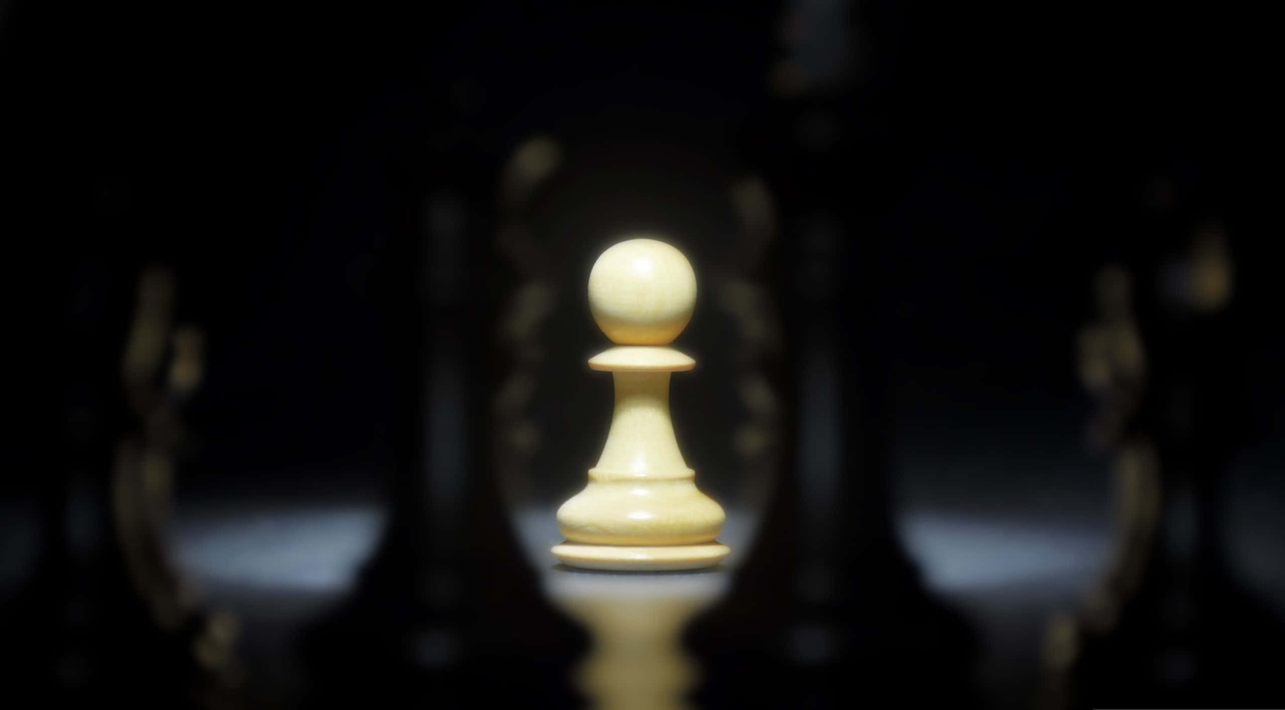 西洋棋 桌布 壁紙 — 一個單獨照亮的白色西洋棋兵在黑暗模糊的背景中，面對著對面的黑色棋子，清晰對焦。