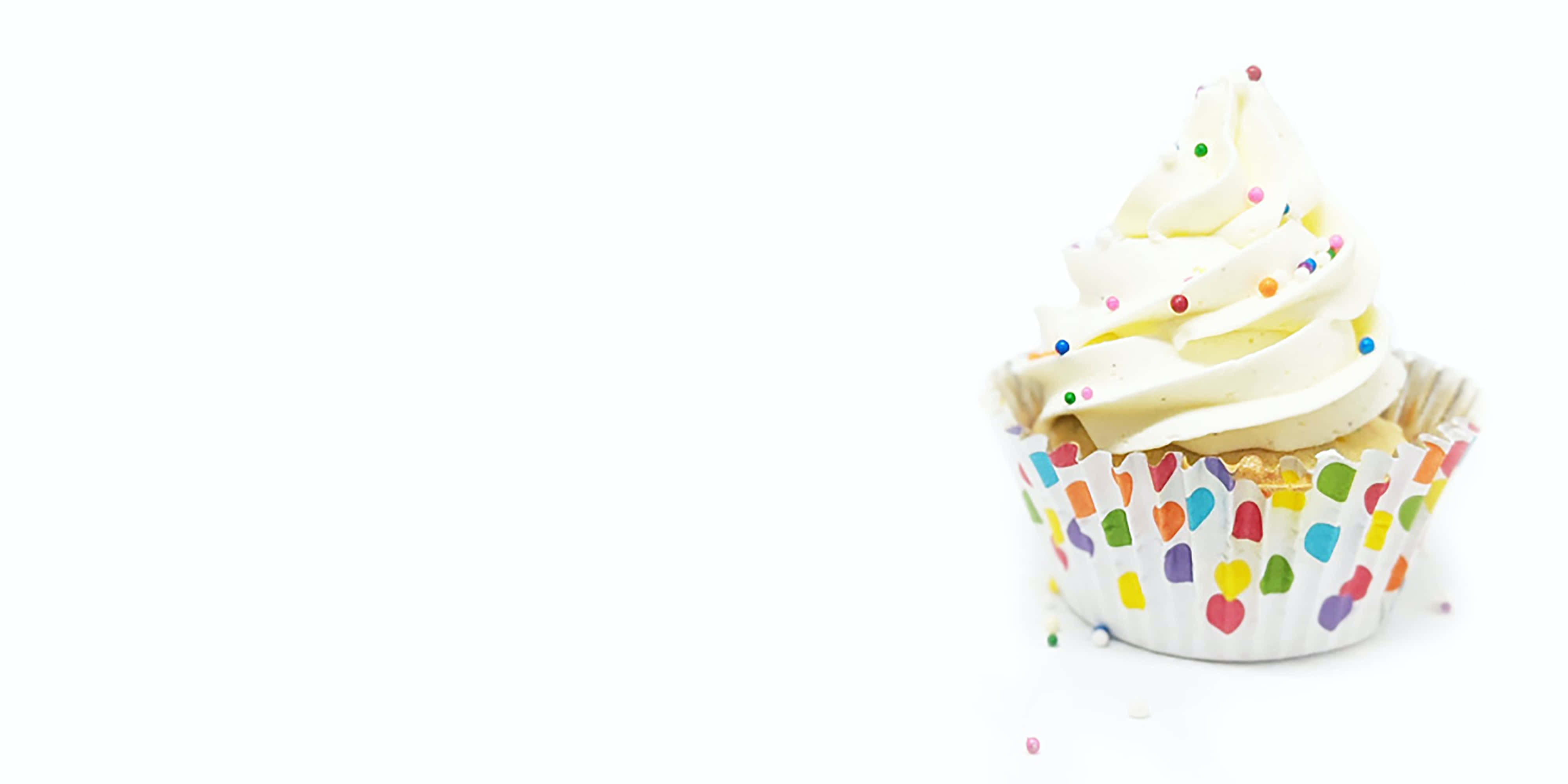 Cupcake 桌布 壁紙 — 一個單獨的杯子蛋糕，上面有白色糖霜和彩色糖粒，放在彩虹圖案的襯紙裡，背景是潔淨的白色。