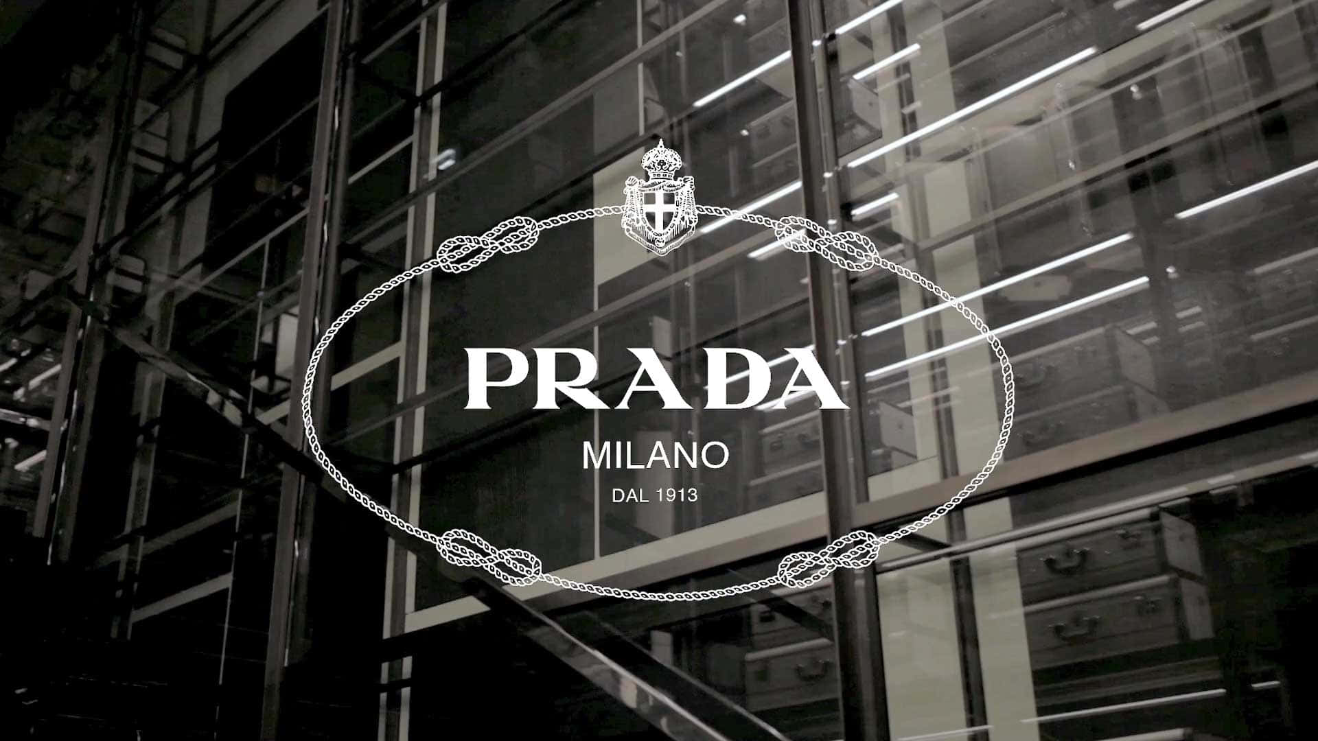 Prada 桌布 壁紙 — 一個單色Prada商店標誌，帶有華麗的鏈條細節，在反射工業室內燈光的玻璃外牆上發光。