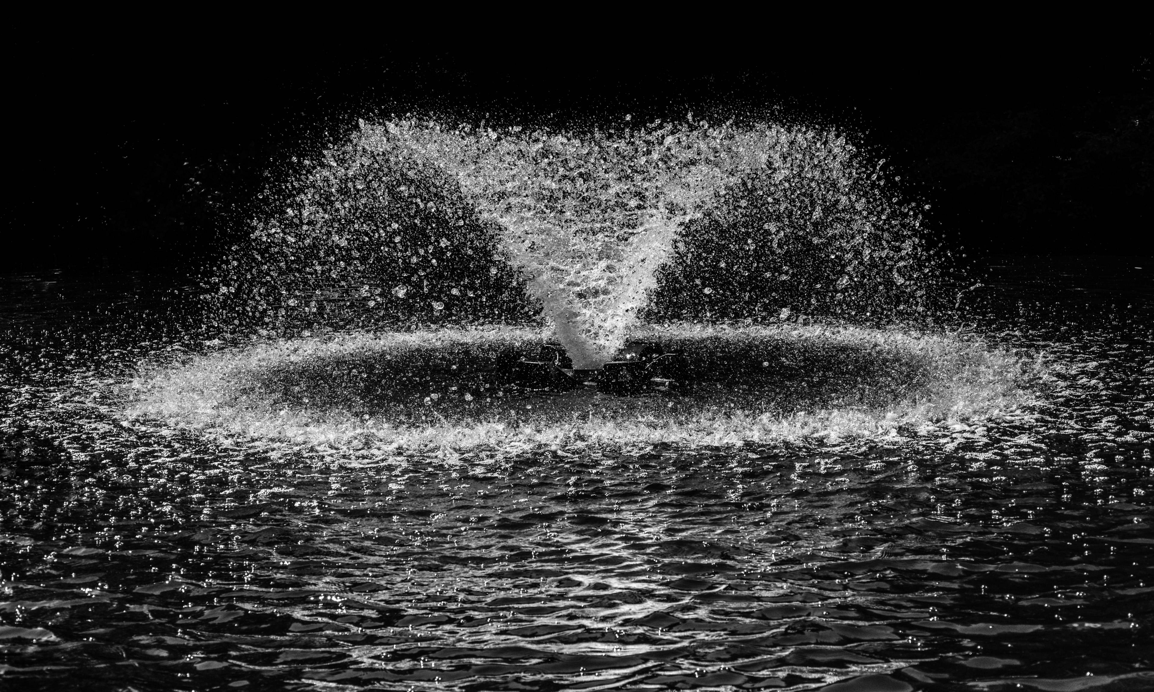 Water Splash 桌布 壁紙 — 一個單色噴泉在黑暗虛空中對稱噴射，捕捉到空中水滴，具有高對比度和清晰細節。