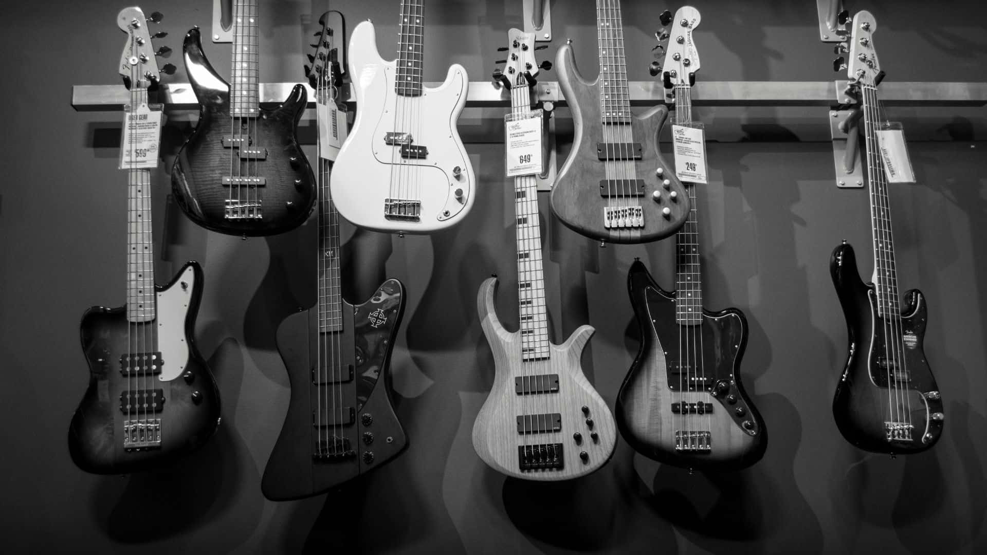 Black And White Guitar 桌布 壁紙 — 一個單色展示，各種低音吉他整齊地掛在音樂店的牆上。