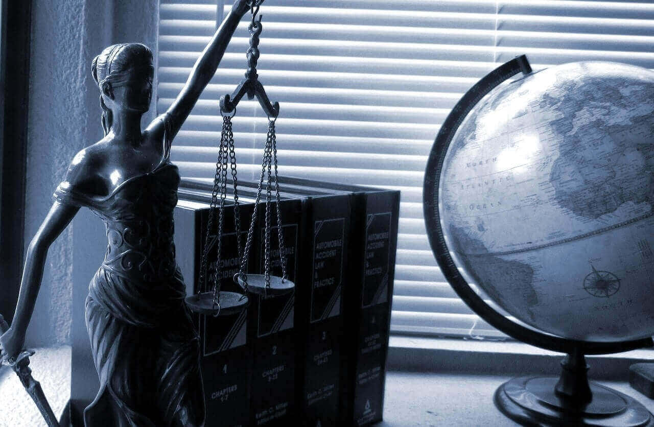 Punitive 桌布 壁紙 — 一個單色正義女神雕像站在窗台上，旁邊有法律書籍和一個地球儀，窗台上有百葉窗。