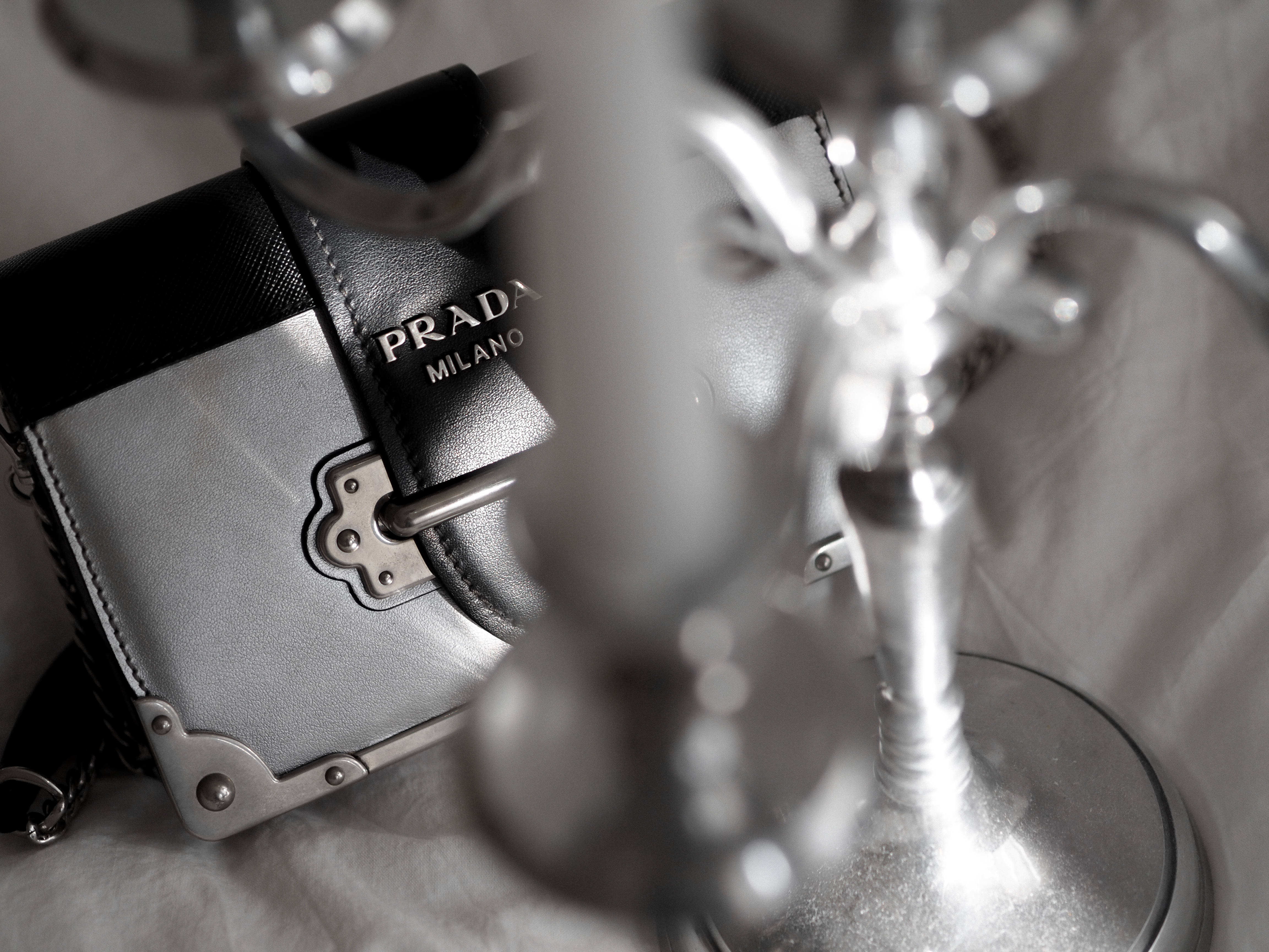 Prada 桌布 壁紙 — 一個單色特寫，Prada Milano 手提包配銀色金屬配件，旁邊放著一個模糊的華麗燭台。
