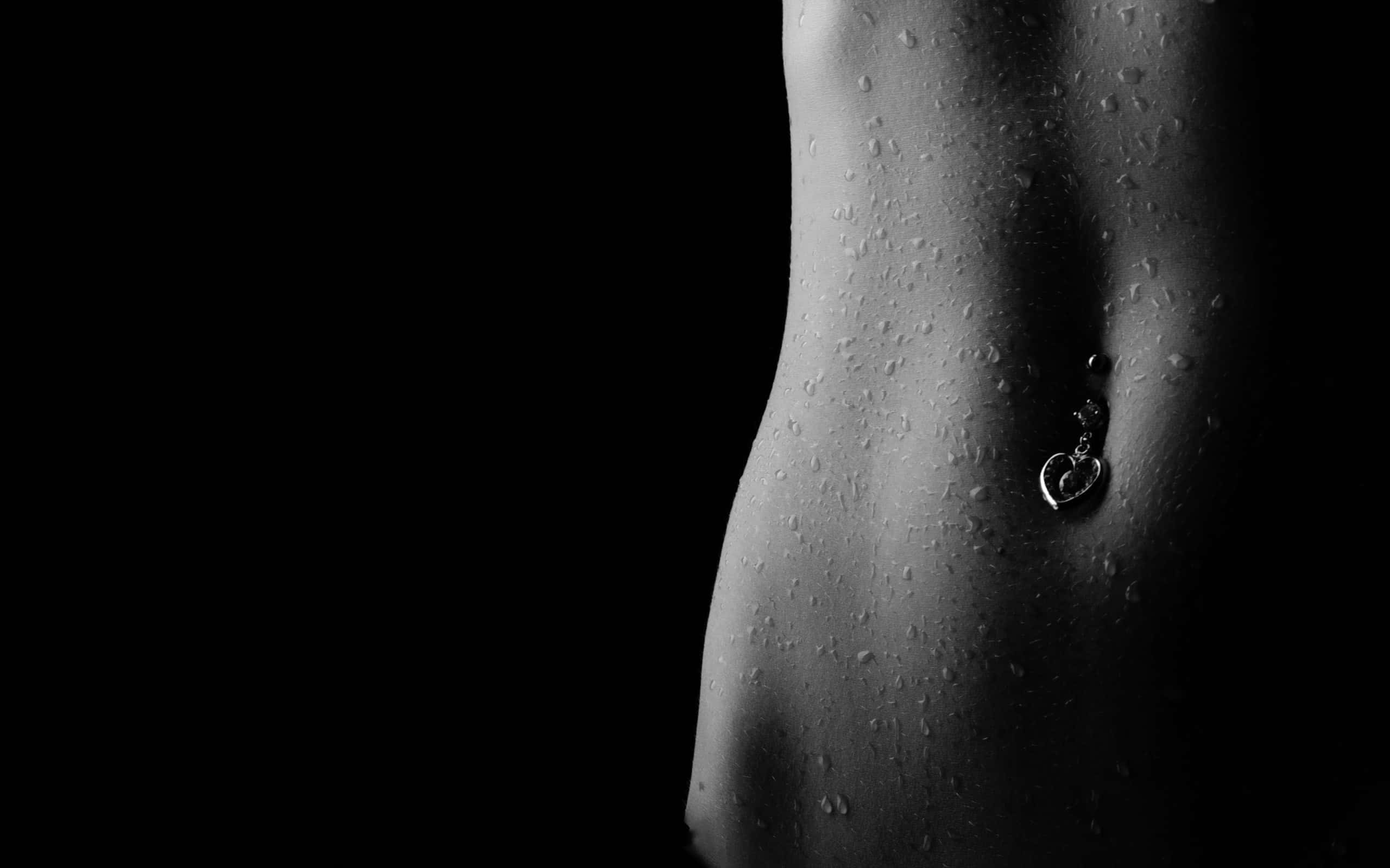 Piercing 桌布 壁紙 — 一個單色特寫，展示濕潤的人類軀幹，帶有肚臍環，背景為純黑色。