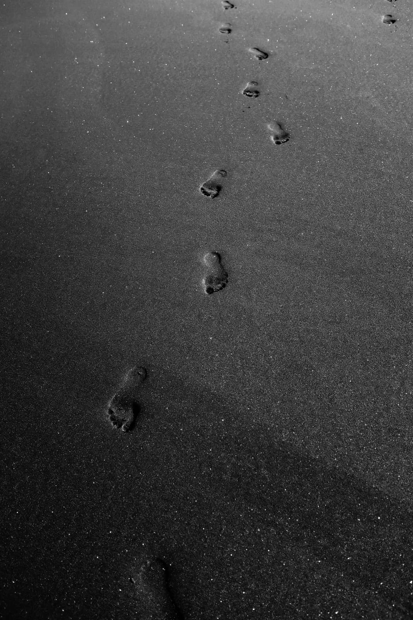 sand 桌布 壁紙 — 一個單色特寫，腳印在濕沙上延伸，逐漸消失在遠方。