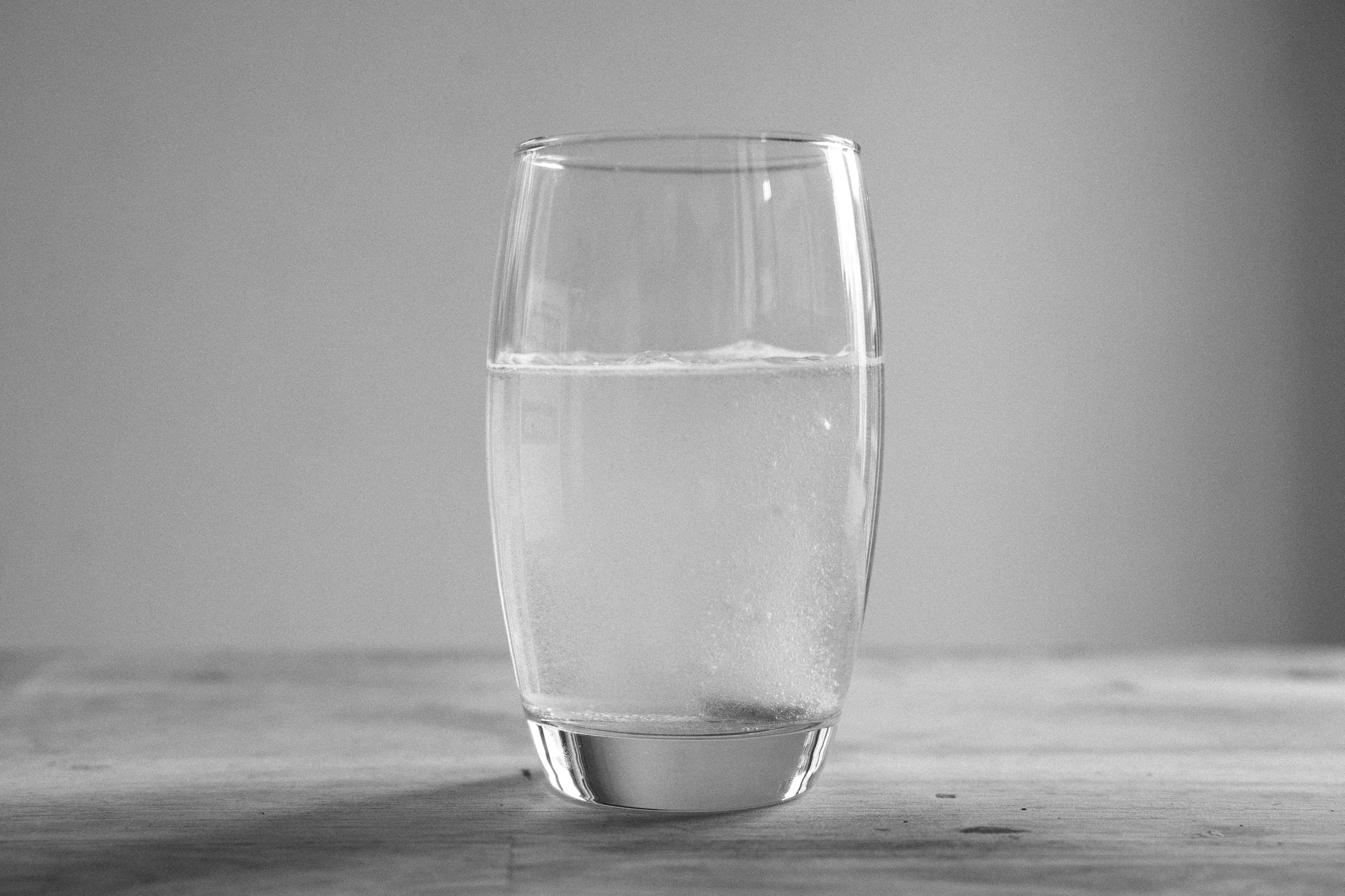 Glass Of Water 桌布 壁紙 — 一個單色玻璃杯裝著氣泡水放在木質表面上，背景柔和模糊。