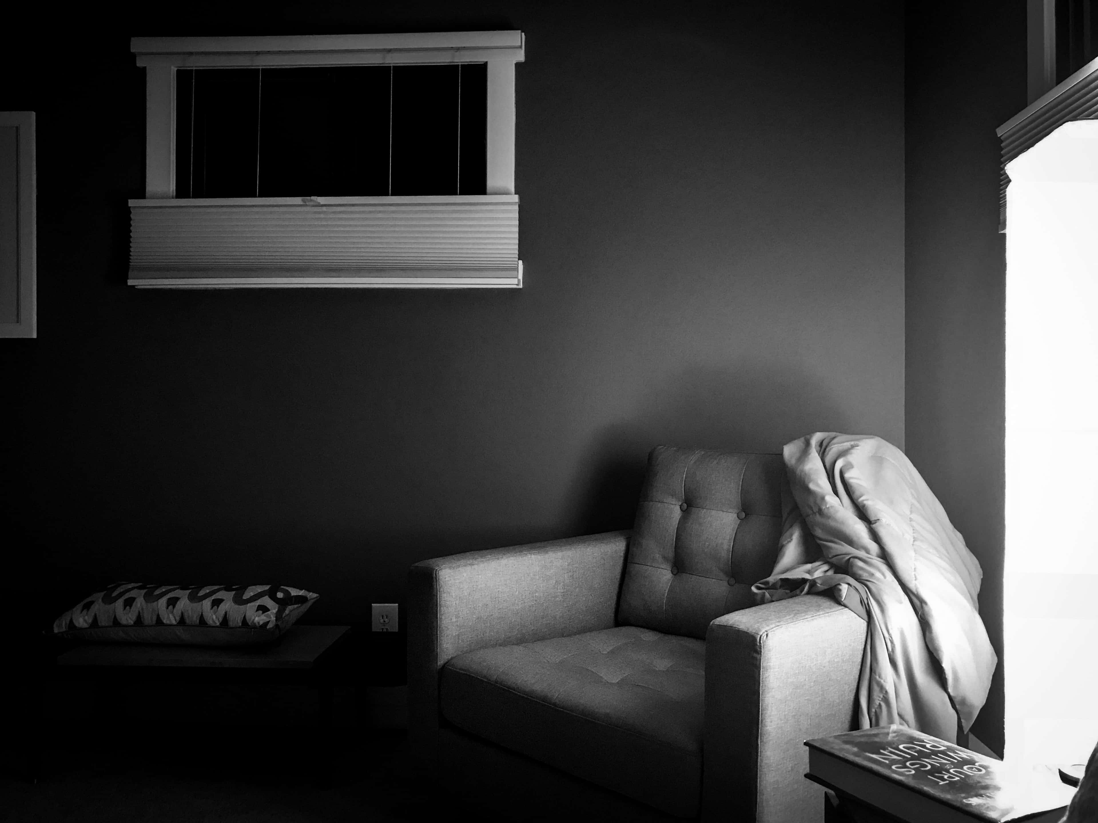 Dark Room 桌布 壁紙 — 一個單色調的室內場景，一張簇絨扶手椅披著毯子，旁邊是帶百葉窗的窗戶，投射出柔和的光線。