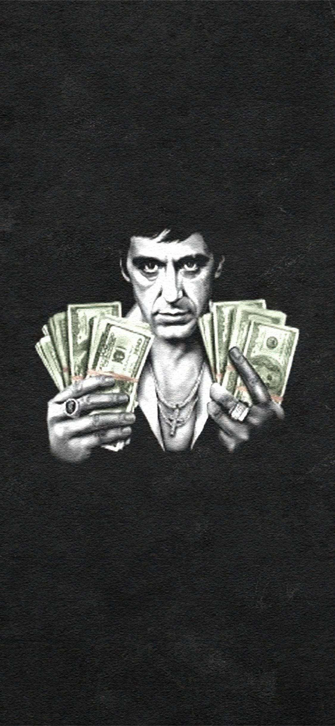 Al Pacino Scarface 桌布 壁紙 — 一個嚴肅的男人穿著深色西裝，在黑色背景前拿著扇狀展開的綠色美元鈔票。