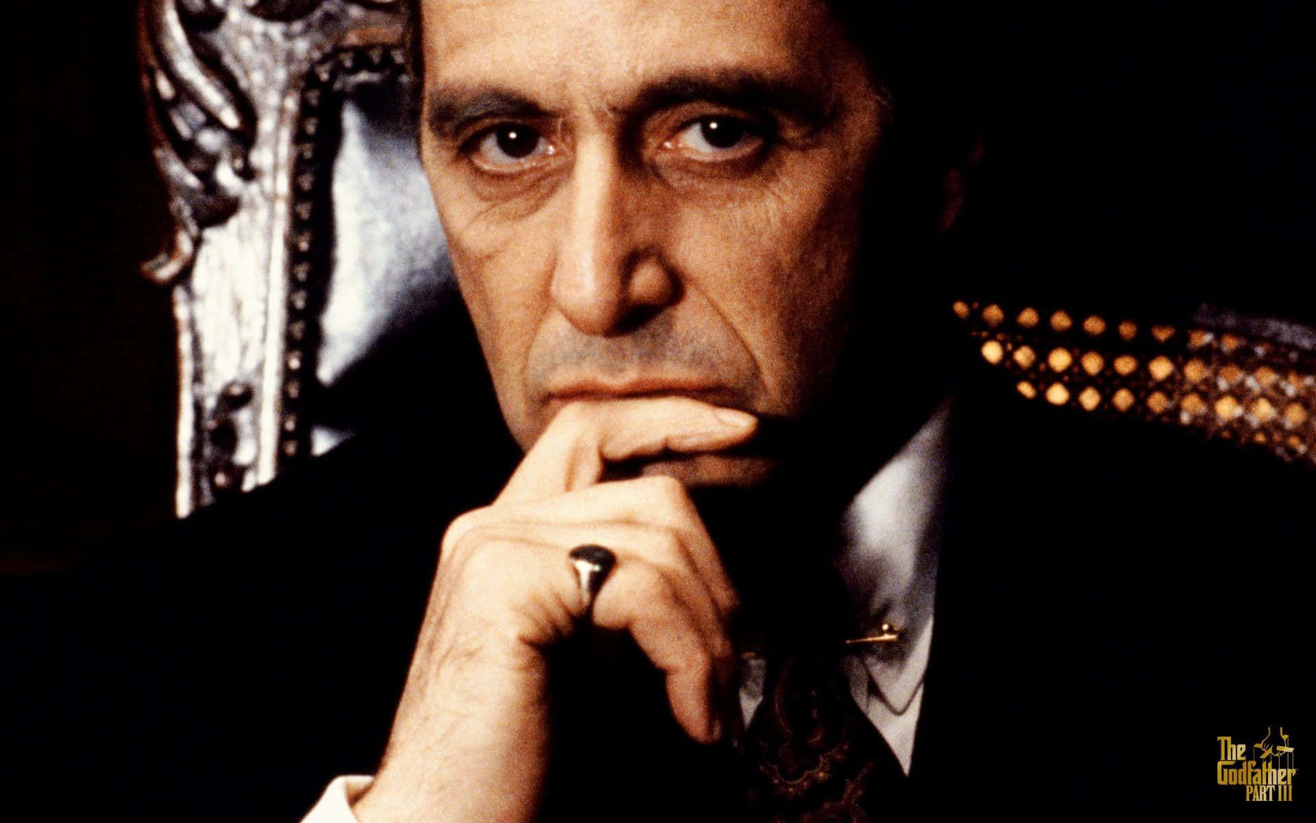 Michael Corleone 桌布 壁紙 — 一個嚴肅的男人穿著深色西裝，將下巴擱在戴著戒指的手上，坐在華麗的椅子上，背景昏暗的特寫。