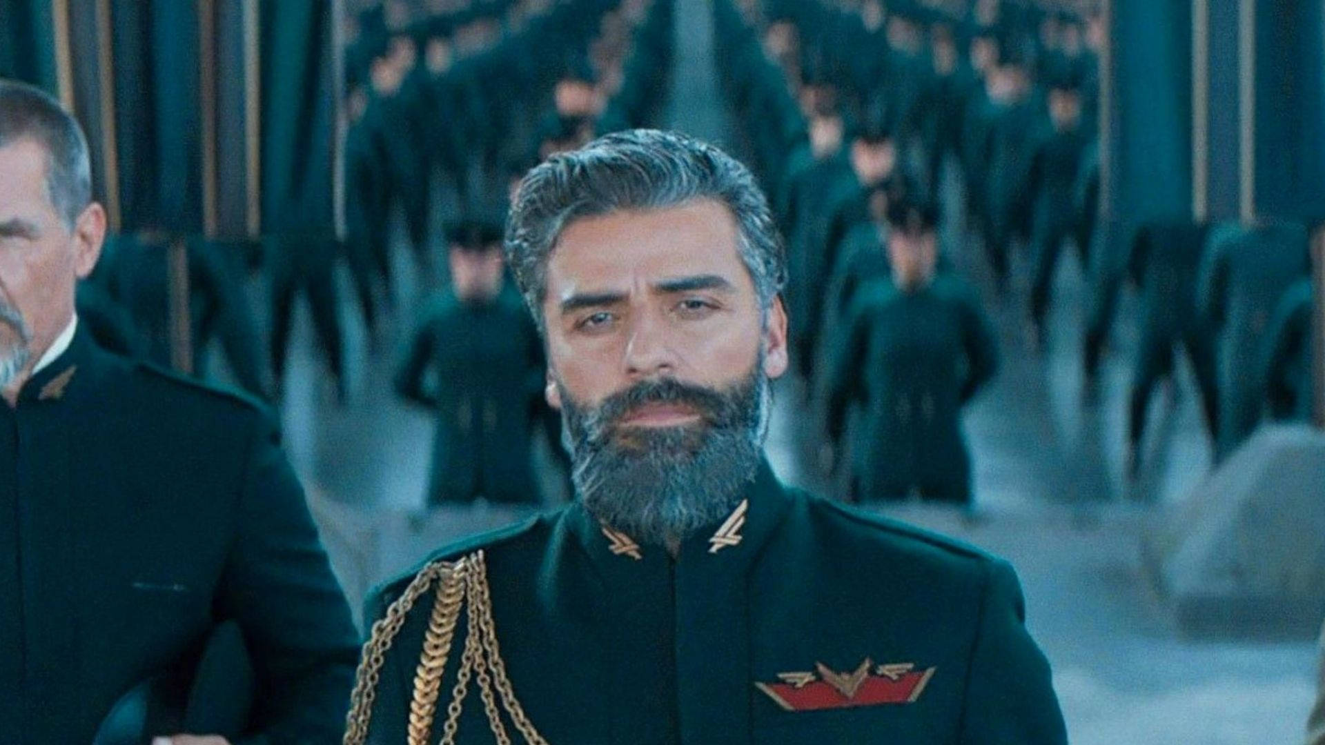 oscar 桌布 壁紙 — 一個嚴肅的鬍鬚男人穿著華麗的深色制服，站在一排相同的士兵前面，在一個昏暗的大廳裡。
