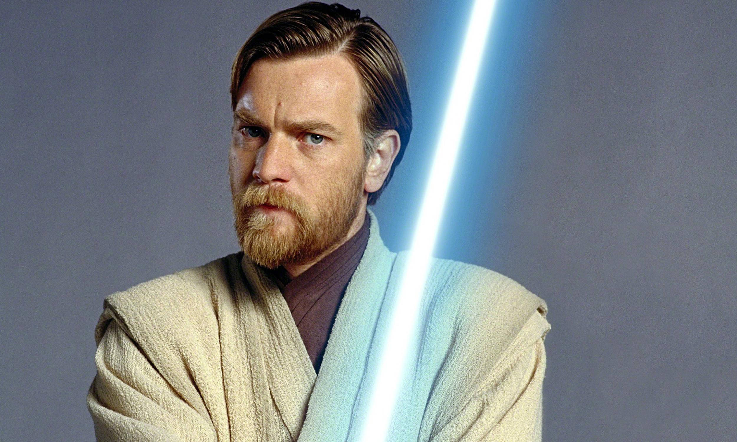 Kenobi 桌布 壁紙 — 一個嚴肅的鬍鬚男穿著淺色長袍，在純灰色背景前拿著發光的藍色光劍。