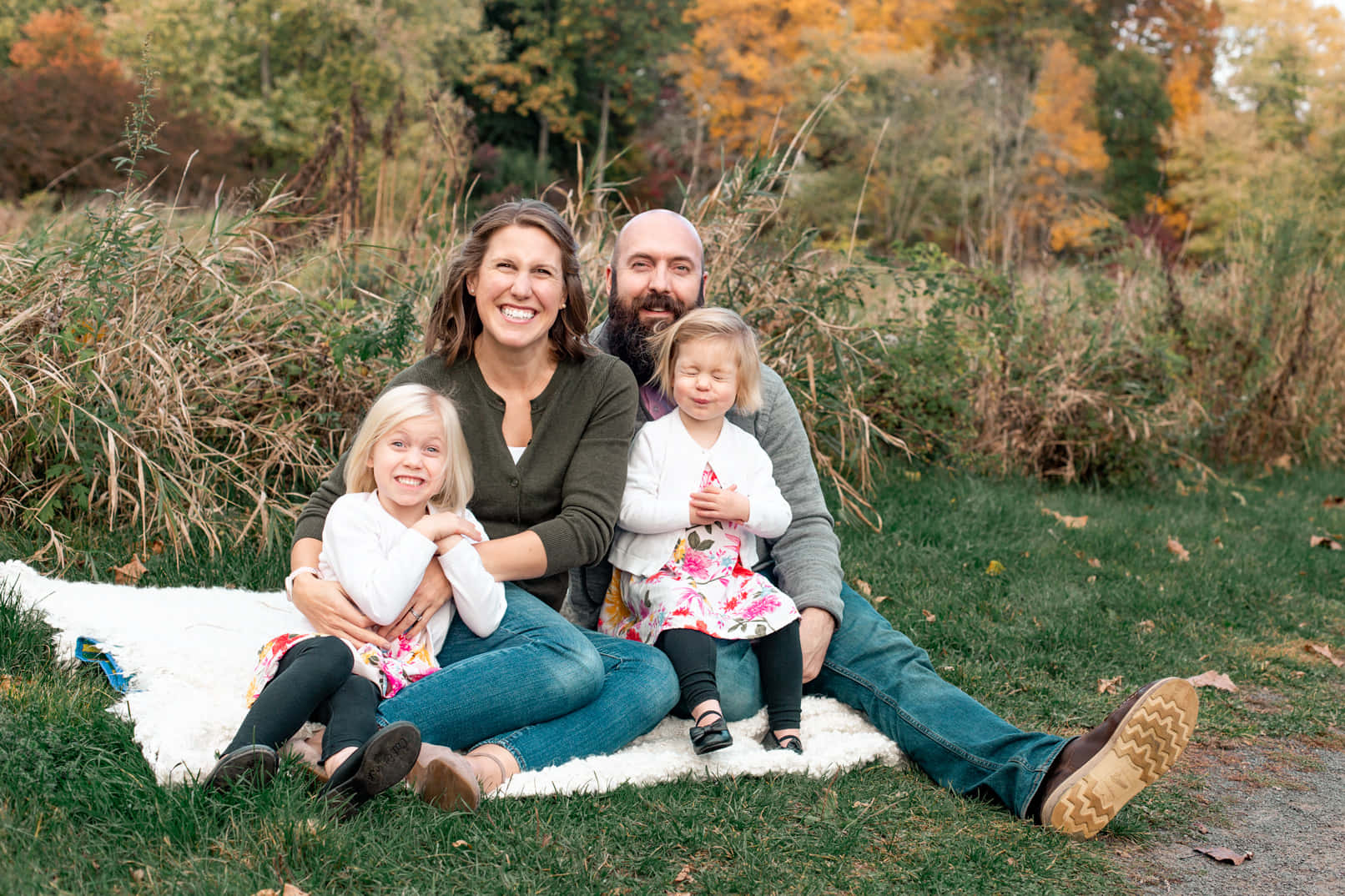 Family 桌布 壁紙 — 一個四口之家微笑著一起坐在草地上的一張白色毯子上，周圍是秋天的樹葉。