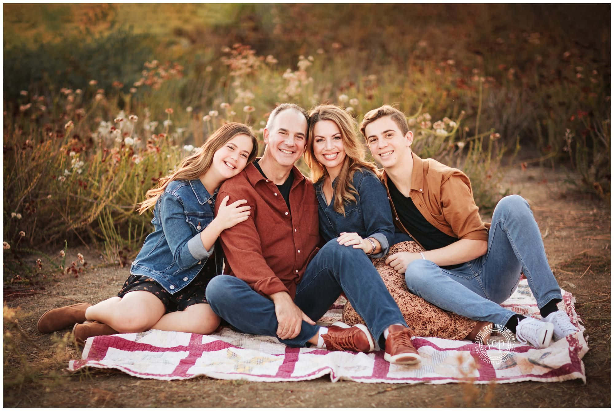 Fall Family 桌布 壁紙 — 一個四口之家微笑著緊密地坐在陽光普照的野花田中的圖案毯子上。