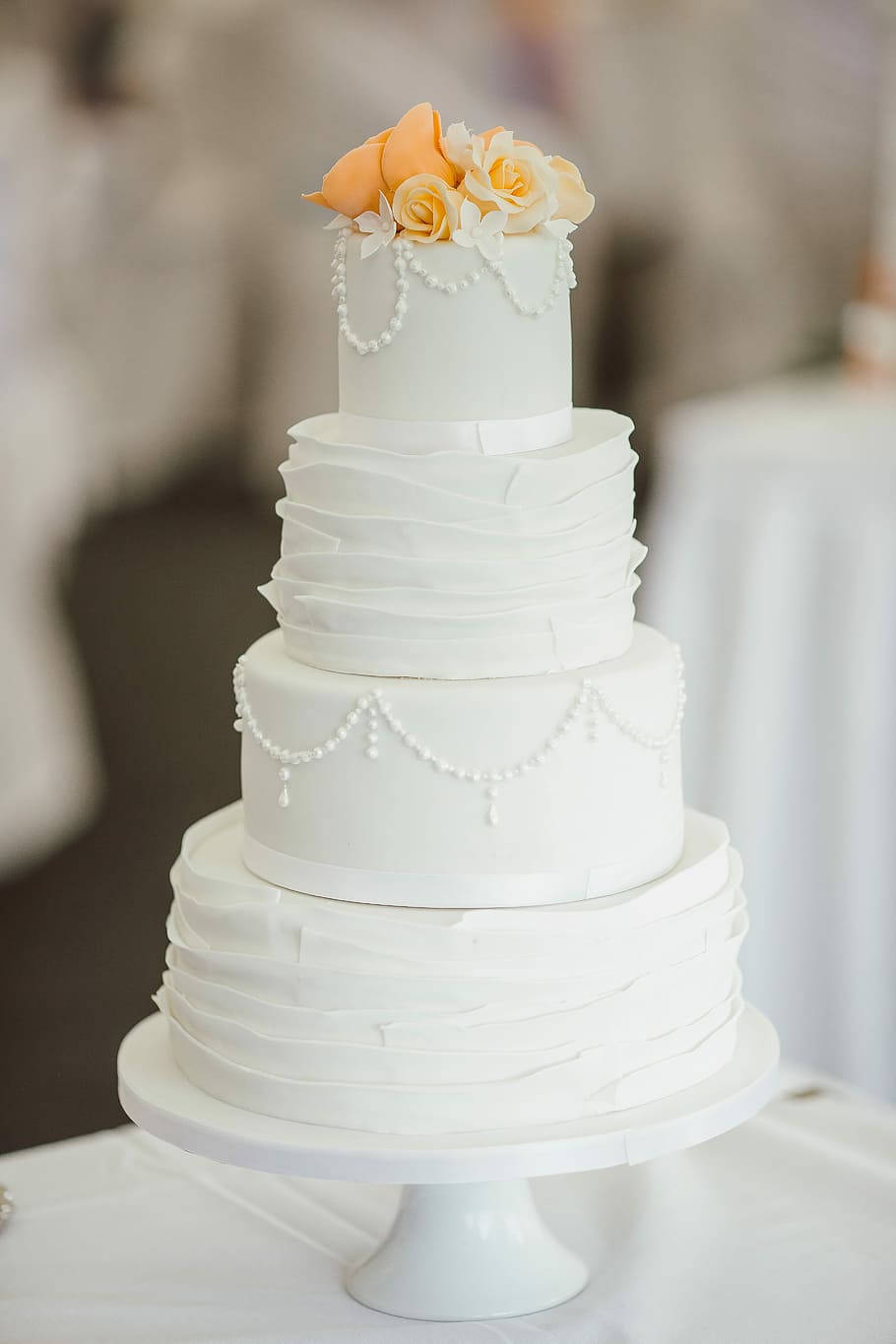 Wedding 桌布 壁紙 — 一個四層白色婚禮蛋糕，飾有蜜桃色和奶油色玫瑰及珍珠裝飾，優雅地放在底座上。