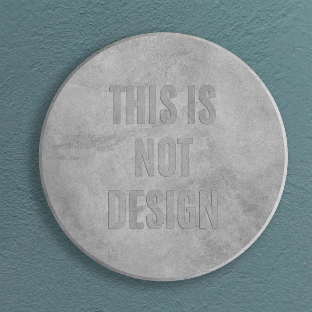 Coin 桌布 壁紙 — 一個圓形混凝土牌，上面有浮雕文字 'THIS IS NOT DESIGN'，安裝在帶紋理的青綠色牆上。