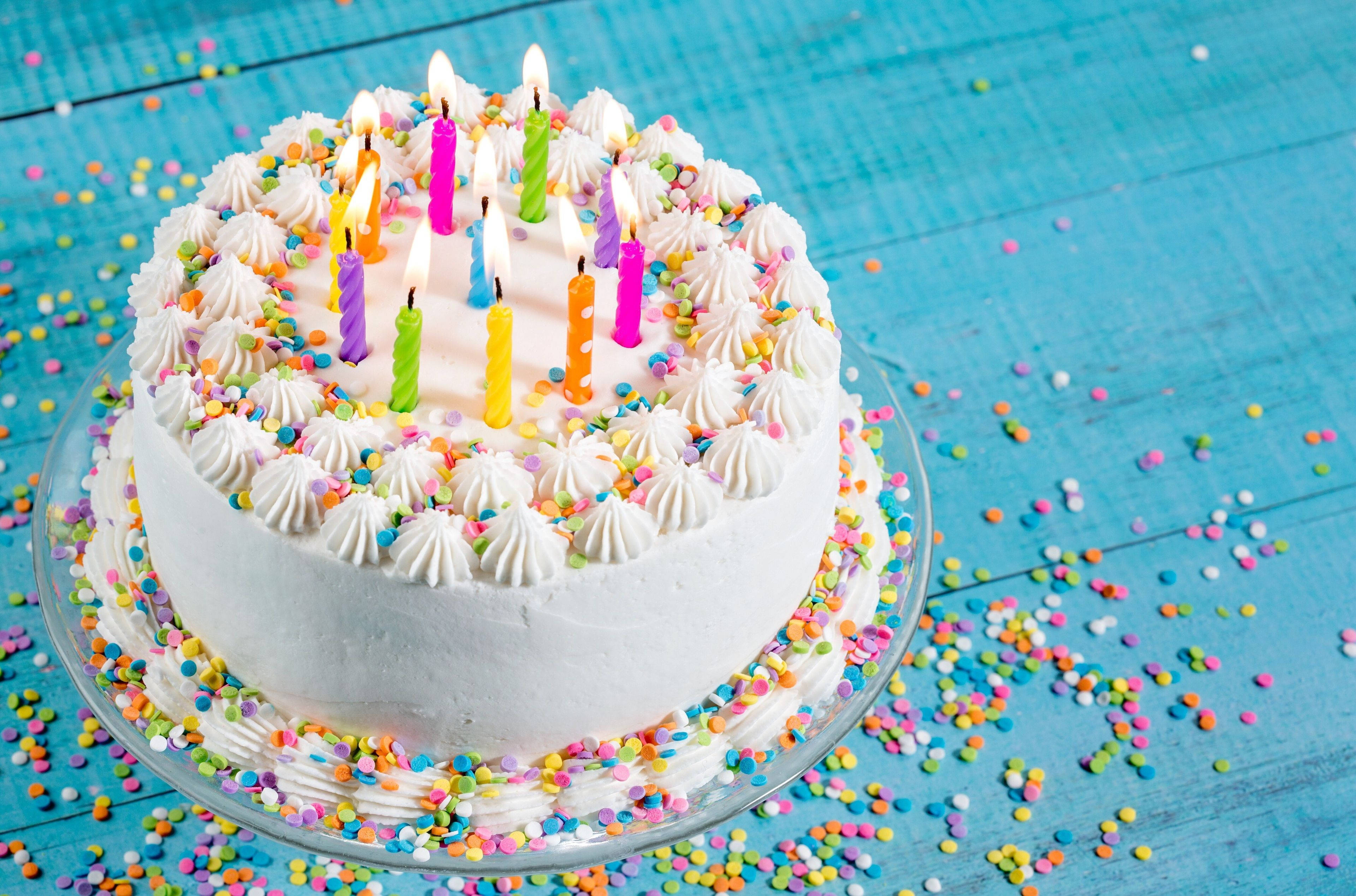 Cake 桌布 壁紙 — 一個圓形生日蛋糕，上面有白色糖霜和彩色蠟燭，放在一個灑滿彩色糖粒的藍色木桌上。