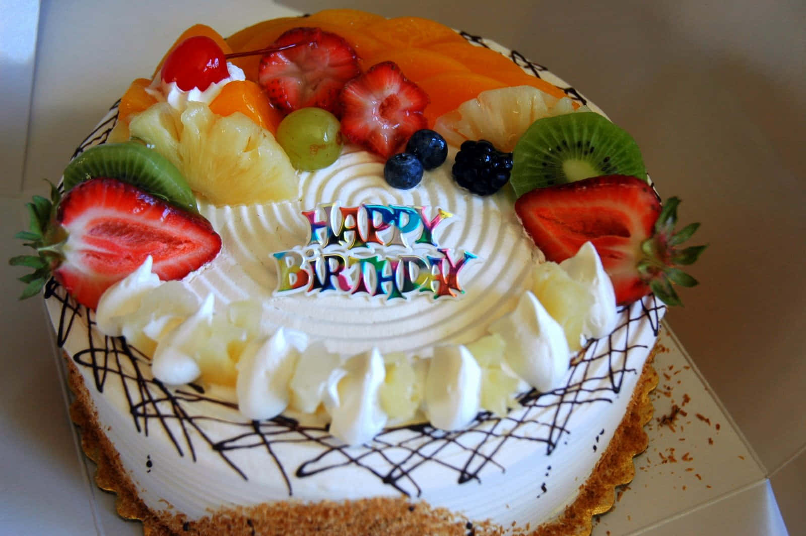 Happy Birthday Cake 桌布 壁紙 — 一個圓形生日蛋糕，上面鋪滿色彩繽紛的新鮮水果，中間插著一支「Happy Birthday」蠟燭。
