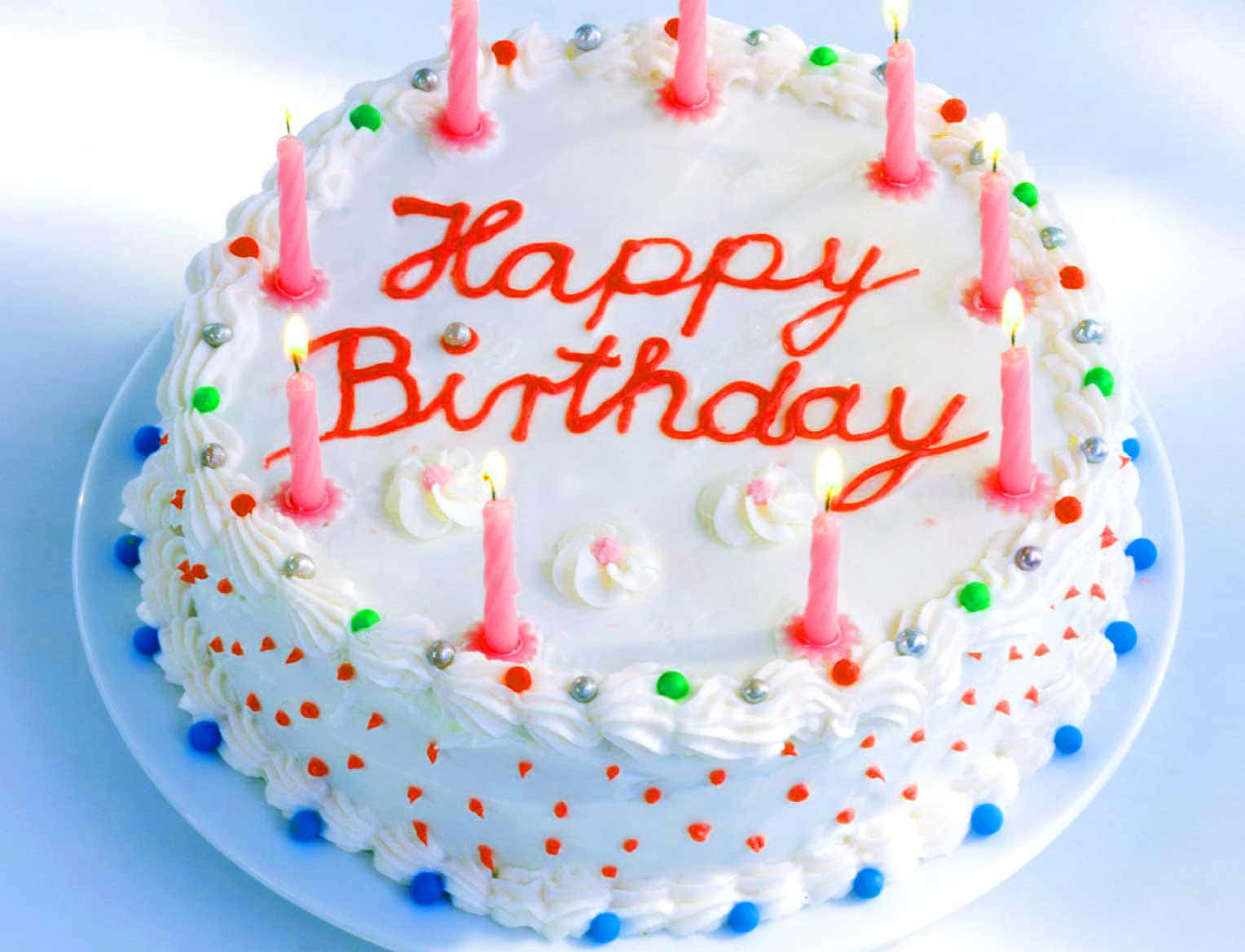 Birthday Cake 桌布 壁紙 — 一個圓形生日蛋糕，有白色糖霜、紅色字樣和點燃的粉紅色蠟燭，周圍佈滿彩色糖粒。