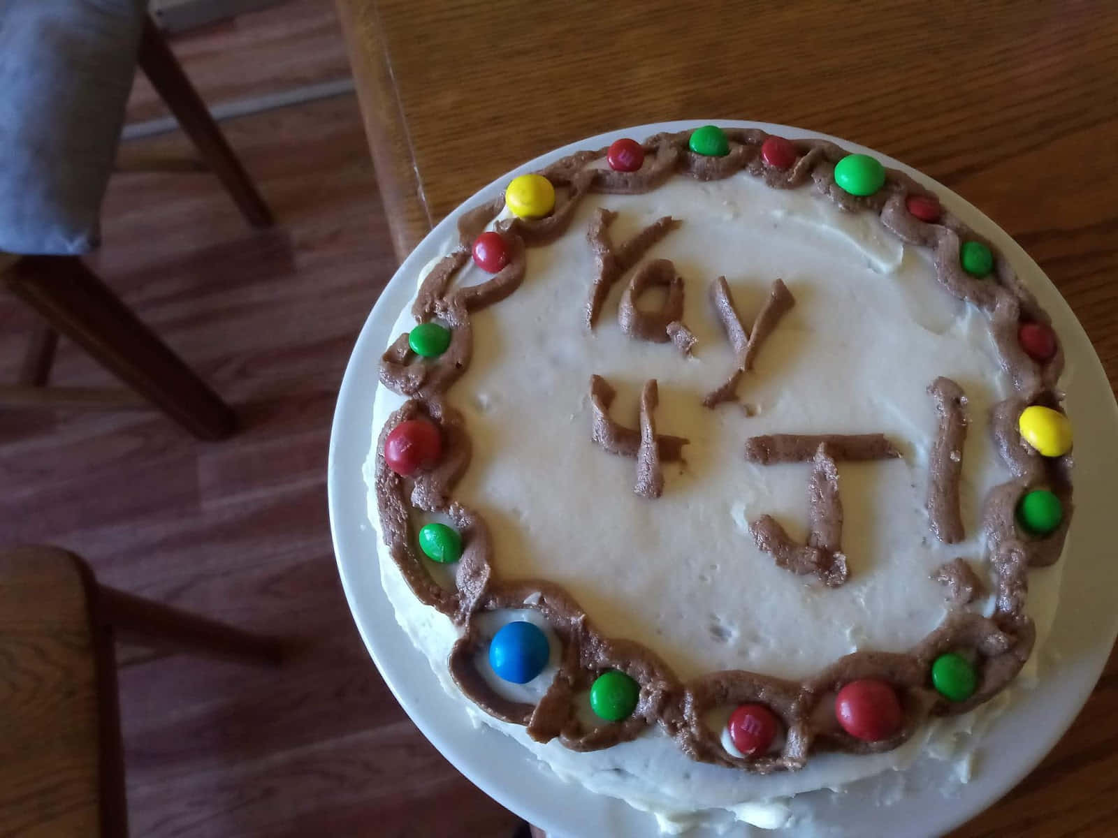 搞笑 桌布 壁紙 — 一個圓形生日蛋糕，白色糖霜，邊緣有彩色M&M's，用巧克力糖霜拼出「Yay 4 J」。