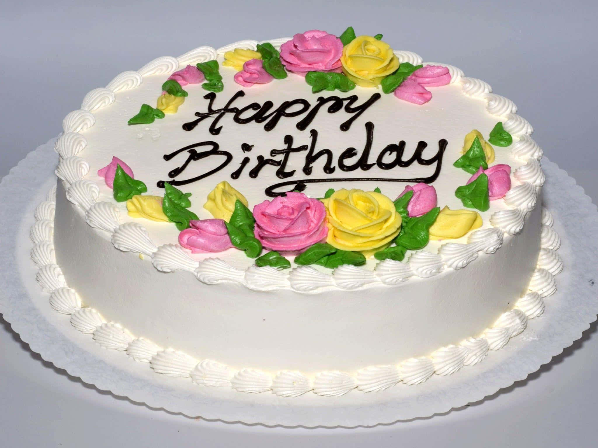 Birthday 桌布 壁紙 — 一個圓形白色生日蛋糕，裝飾有粉紅色和黃色的糖霜玫瑰和綠色葉子，並用黑色糖霜寫上「Happy Birthday」。