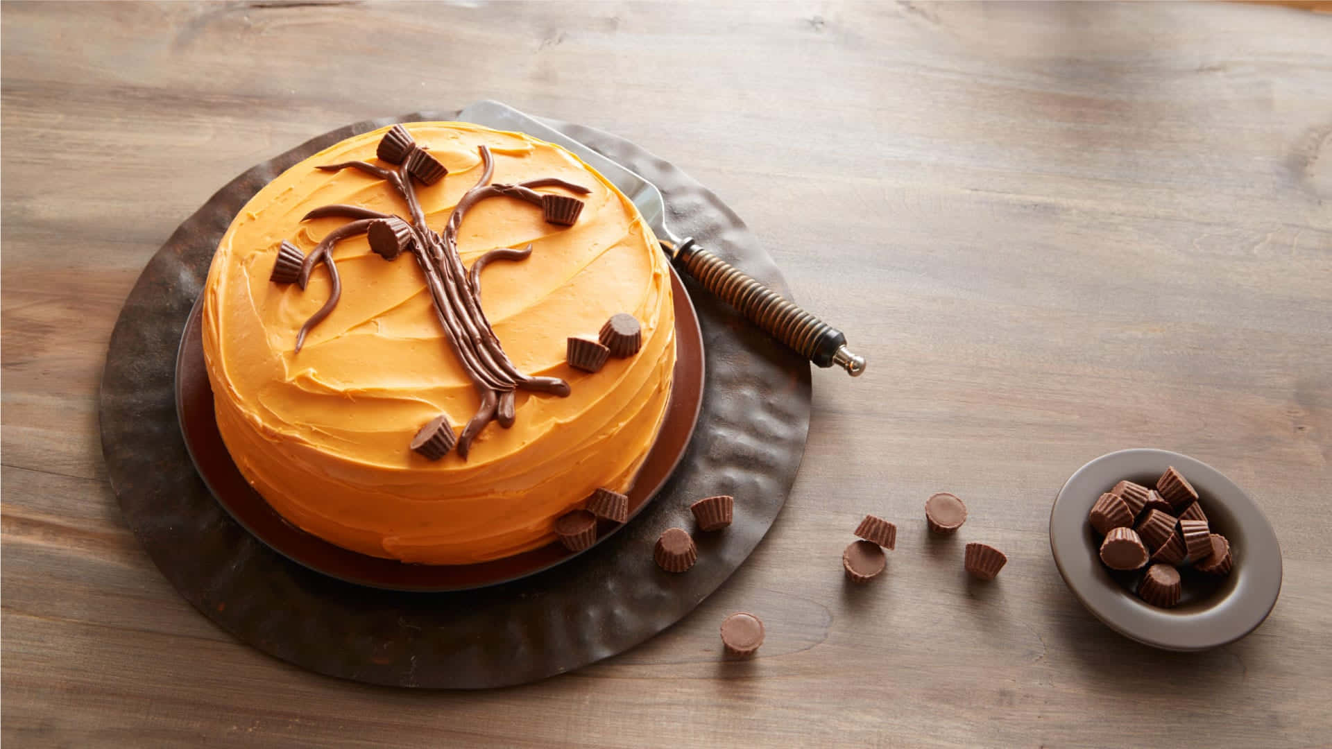 Halloween Cake 桌布 壁紙 — 一個圓形的橙色糖霜蛋糕，裝飾著巧克力樹枝和花生醬杯，放在木桌上。