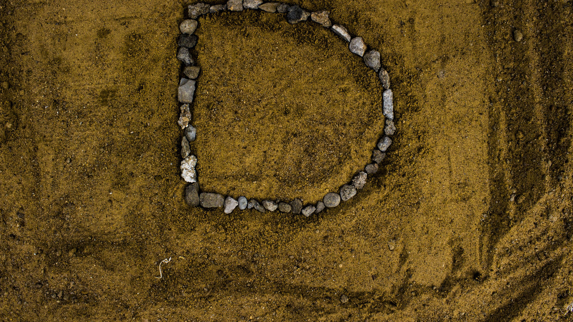 字母D 桌布 壁紙 — 一個圓形石頭排列在自然光下於有紋理的棕色泥土上形成一個完美的環。