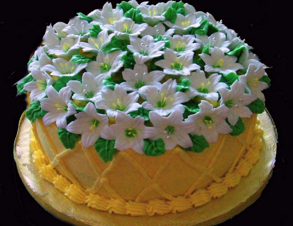 Spring Desserts 桌布 壁紙 — 一個圓形蛋糕，在黑色背景上以金色底座裝飾著白色糖花和綠葉。