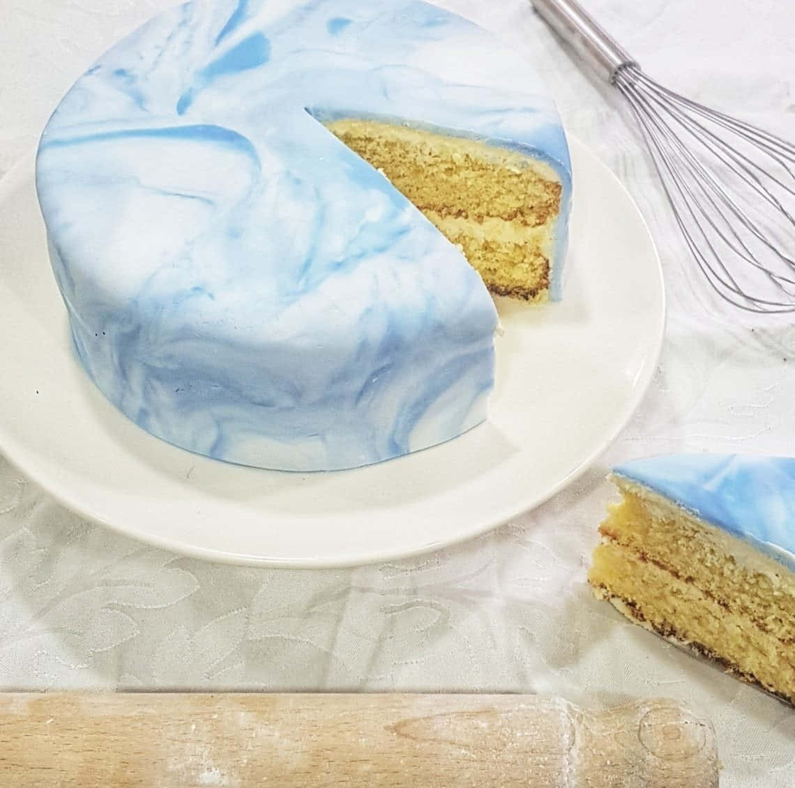 Cake Fondant 桌布 壁紙 — 一個圓形蛋糕，帶有藍白大理石紋糖霜，放在白色盤子上，切掉一塊露出金色海綿蛋糕層。