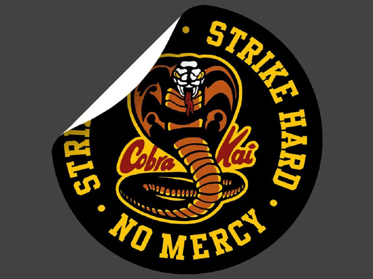 眼鏡蛇道館 桌布 壁紙 — 一個圓形貼紙被撕開，露出一條帶有「Strike Hard No Mercy」粗體黃色和紅色文字的威脅性眼鏡蛇。
