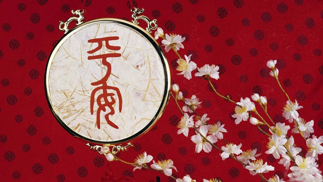 新年 桌布 壁紙 — 一個圓形金框書法作品，上面有紅色漢字，放在帶有黑色圖案的紅色布料上，並飾以精緻的粉紅色櫻花。