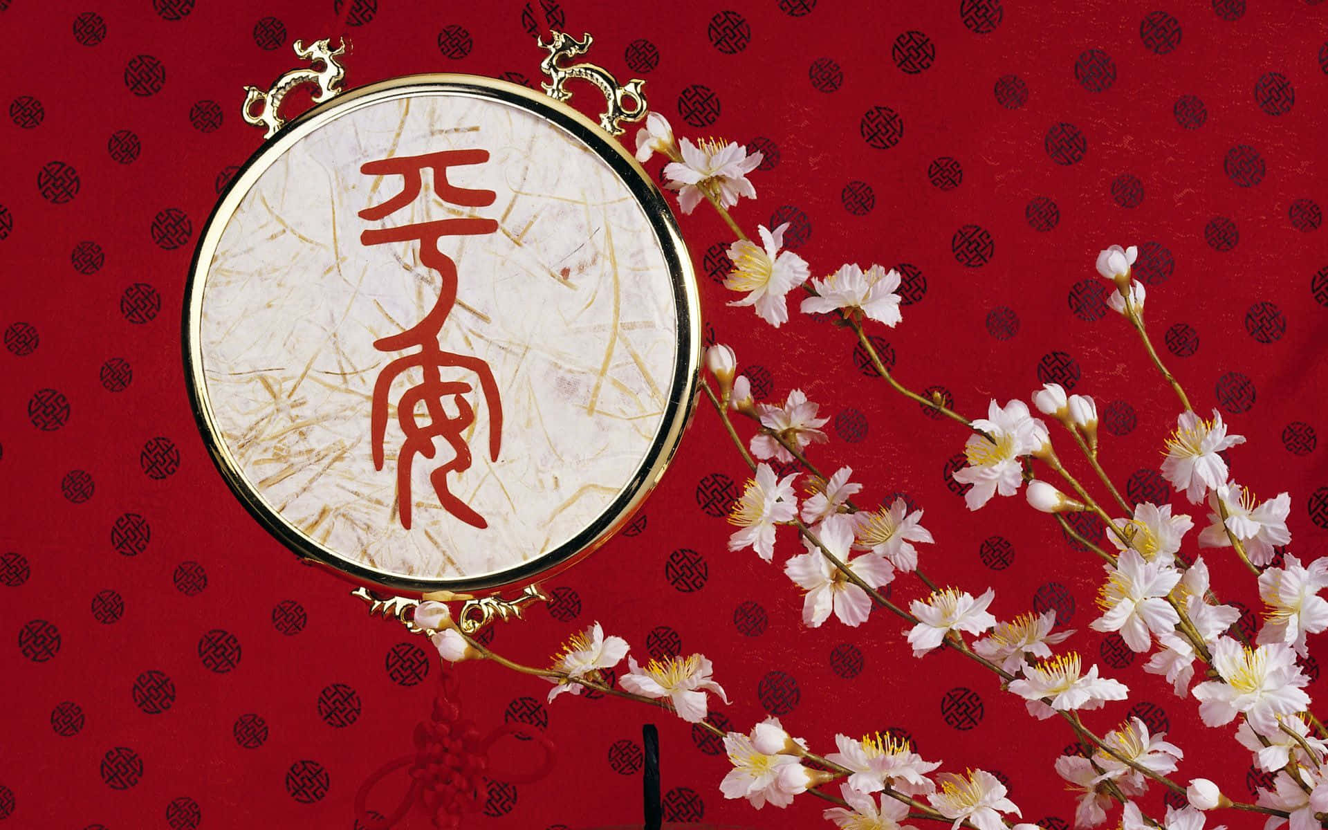 春節 桌布 壁紙 — 一個圓形金框書法牌匾，上面有紅色漢字，放置在一個飾有精緻白色櫻花的紅色圖案背景上。