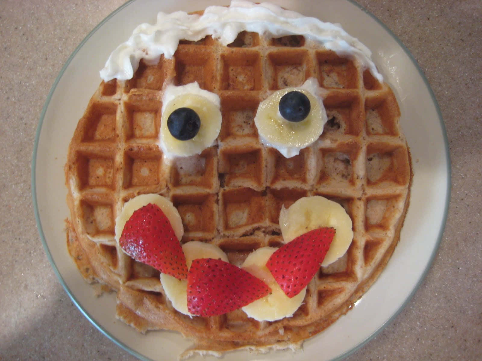 Waffle 桌布 壁紙 — 一個圓形鬆餅，裝飾著鮮奶油、藍莓、香蕉片和草莓，形成一個歡樂的笑臉。
