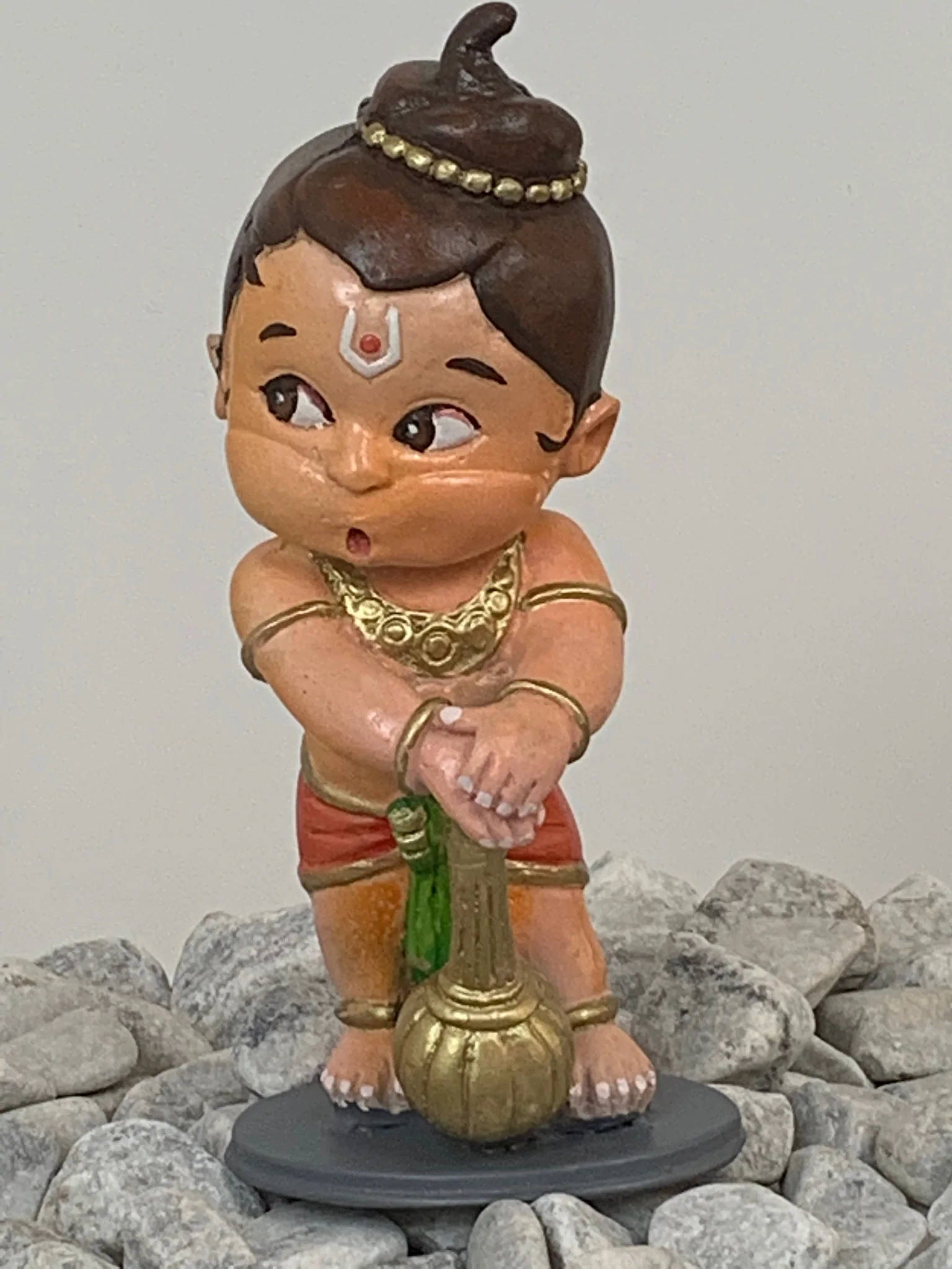 Bal 桌布 壁紙 — 一個圓潤的印度教神像，戴著金飾和髮髻，站在被灰色岩石包圍的基座上。