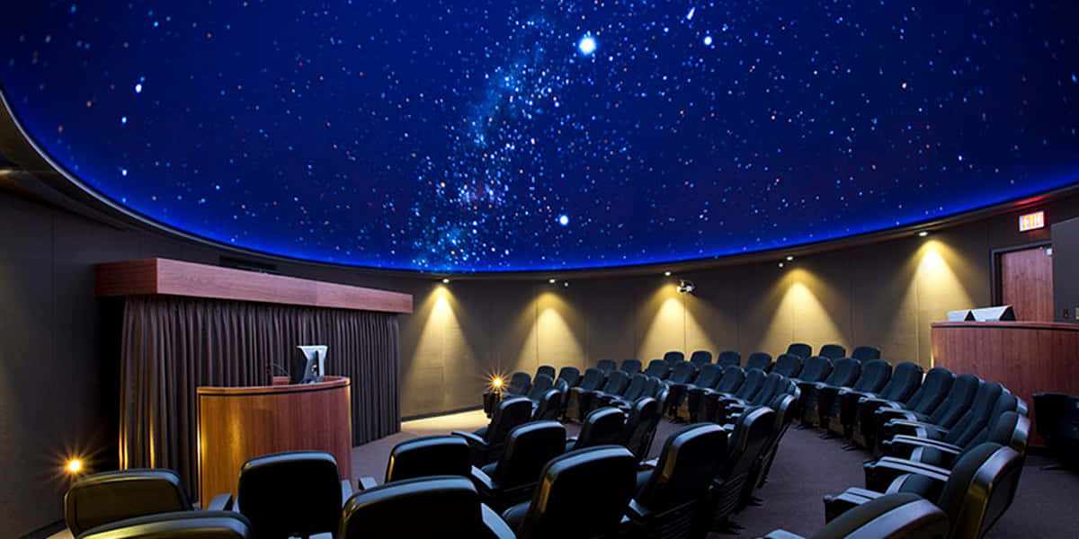 Planetarium 桌布 壁紙 — 一個圓頂天文館劇院，黑色座位排列成行，面向天花板上繁星點點的夜空投影。