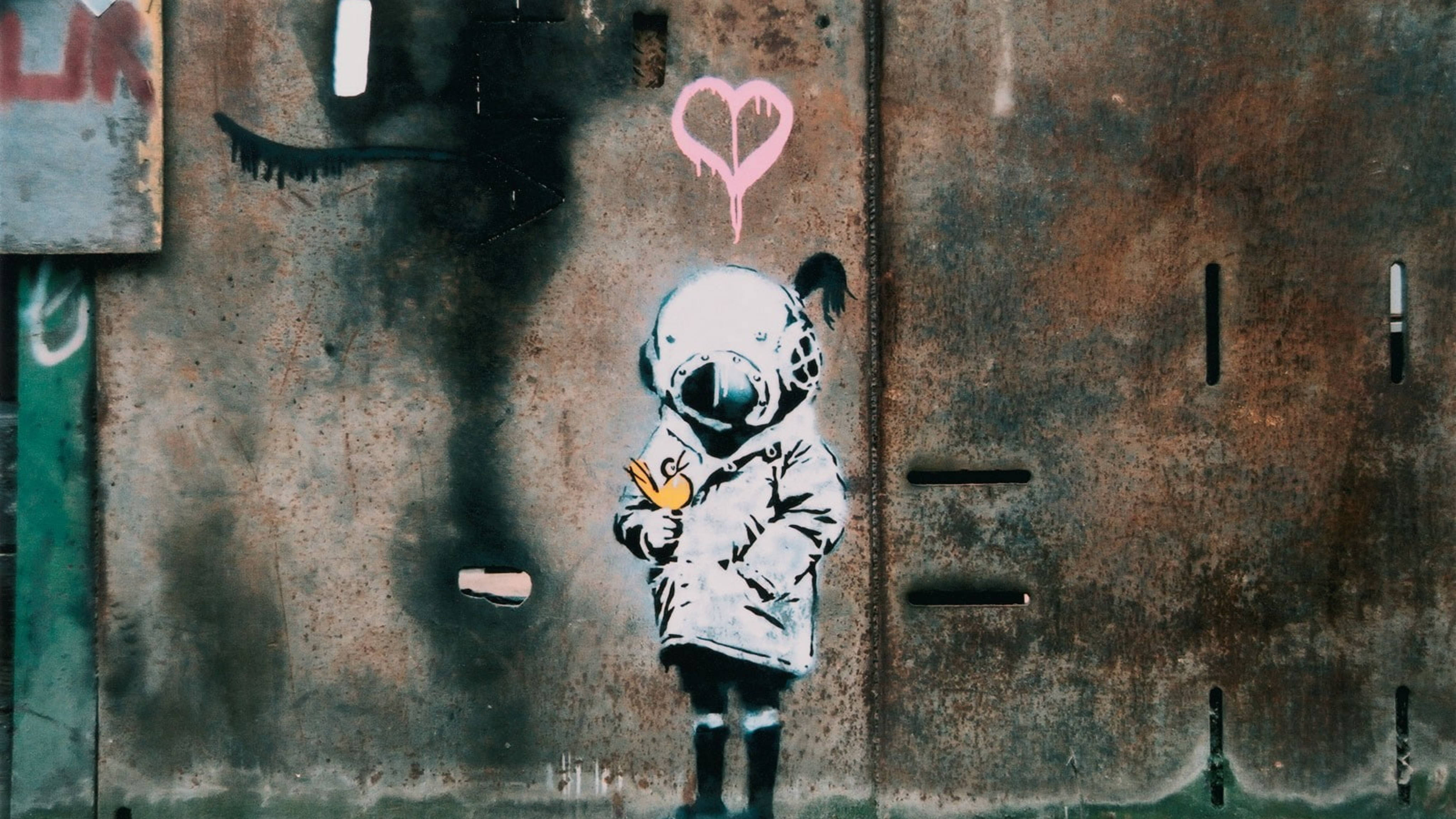Banksy 桌布 壁紙 — 一個在生鏽金屬牆上的模板塗鴉，描繪一個穿著太空衣的小孩，手持一隻黃色小鳥，上方有一個粉紅色心形。
