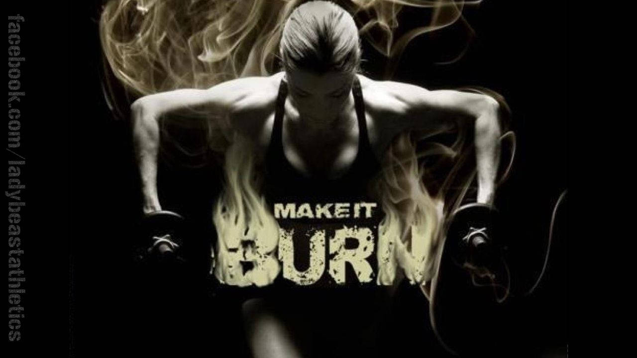 Fitness 桌布 壁紙 — 一個堅定的女人舉起啞鈴，火焰和煙霧在她軀幹周圍旋轉，粗體文字「MAKE IT BURN」以火熱的字體發光。