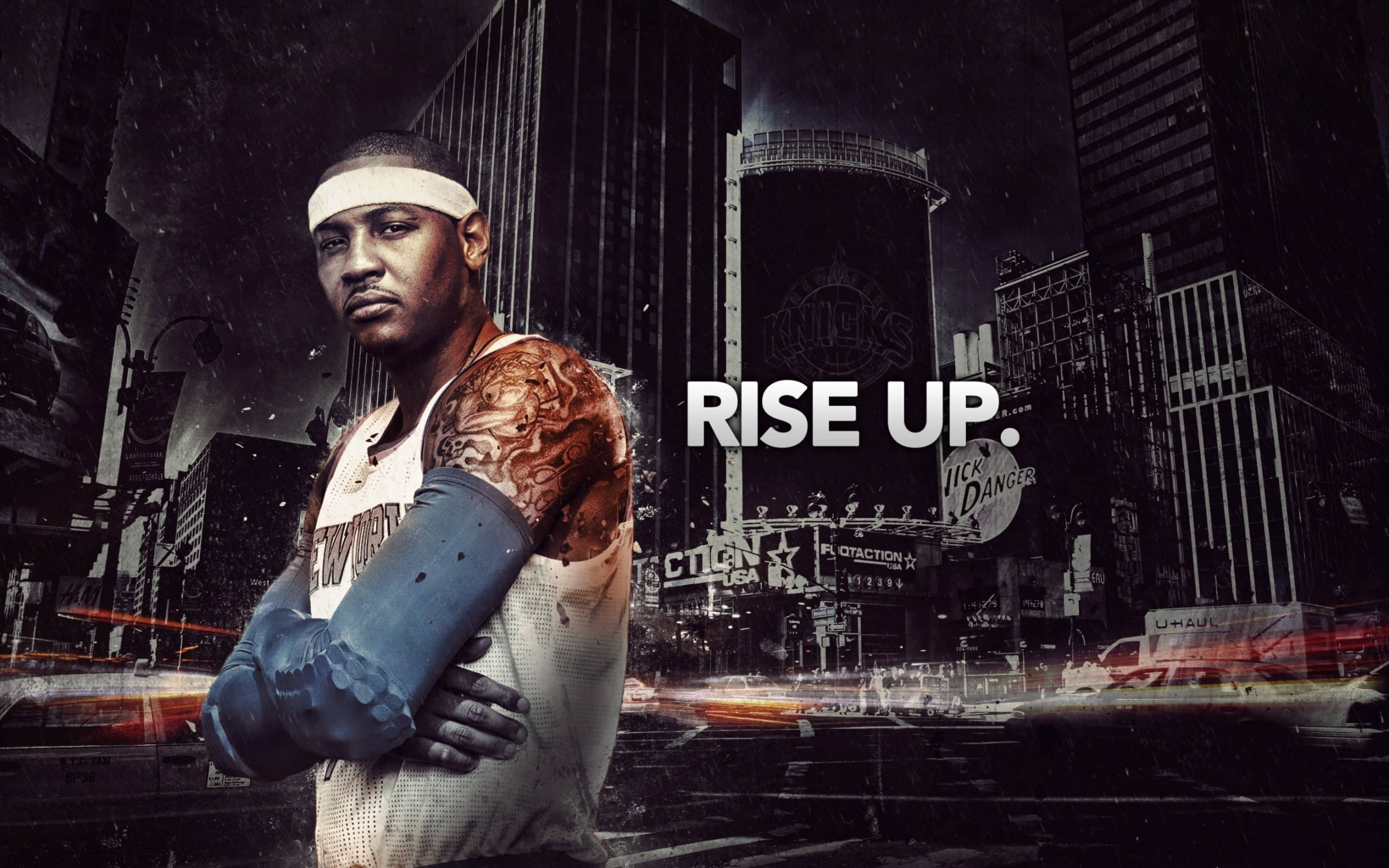 Carmelo 桌布 壁紙 — 一個堅定的籃球運動員，身上有刺青和頭帶，站在雨濕的都市夜景中，背景是模糊的城市燈光和廣告看板。
