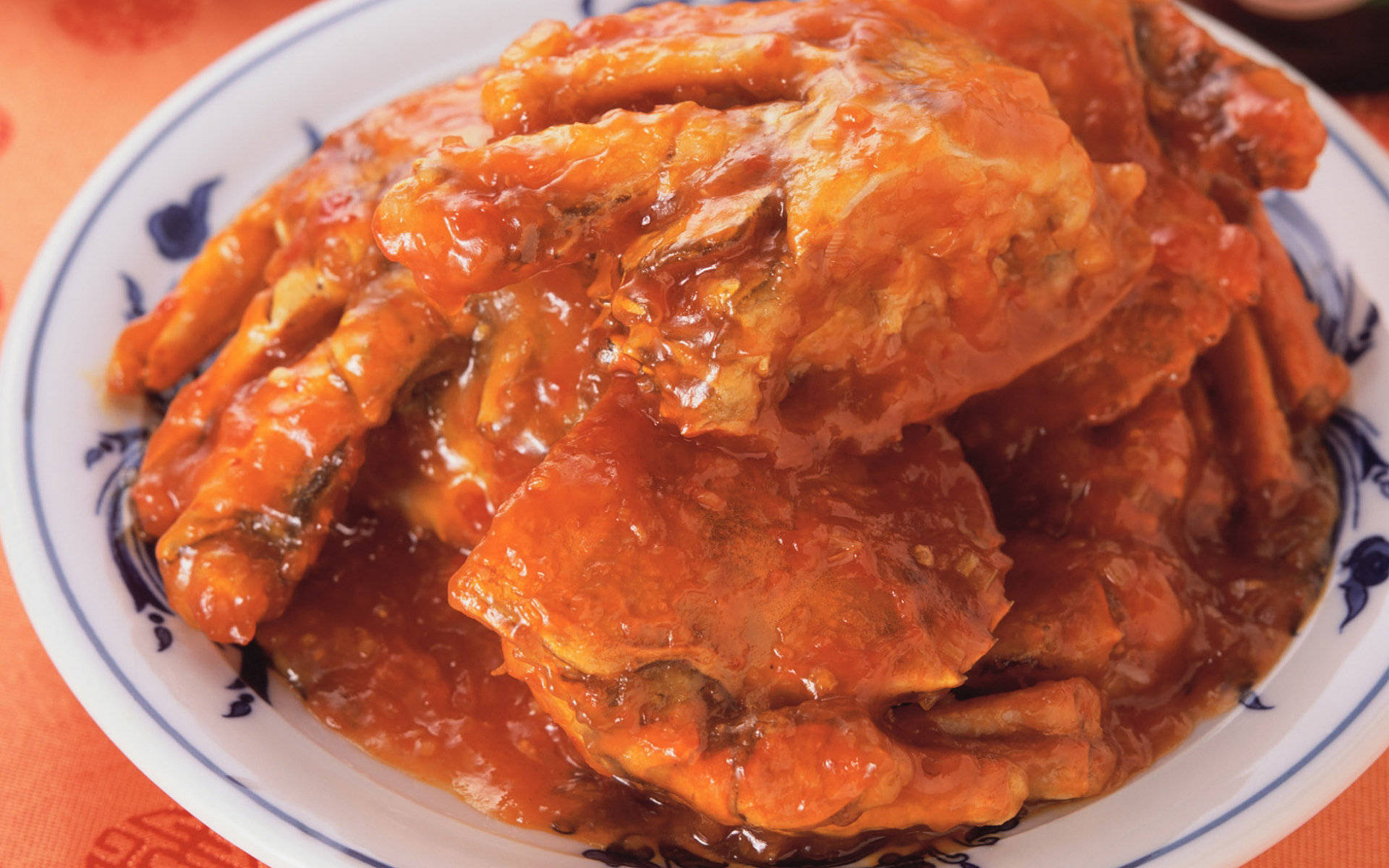 4K Food 桌布 壁紙 — 一個堆滿了閃亮橙色蟹塊、淋上濃郁美味醬汁的藍白陶瓷盤。