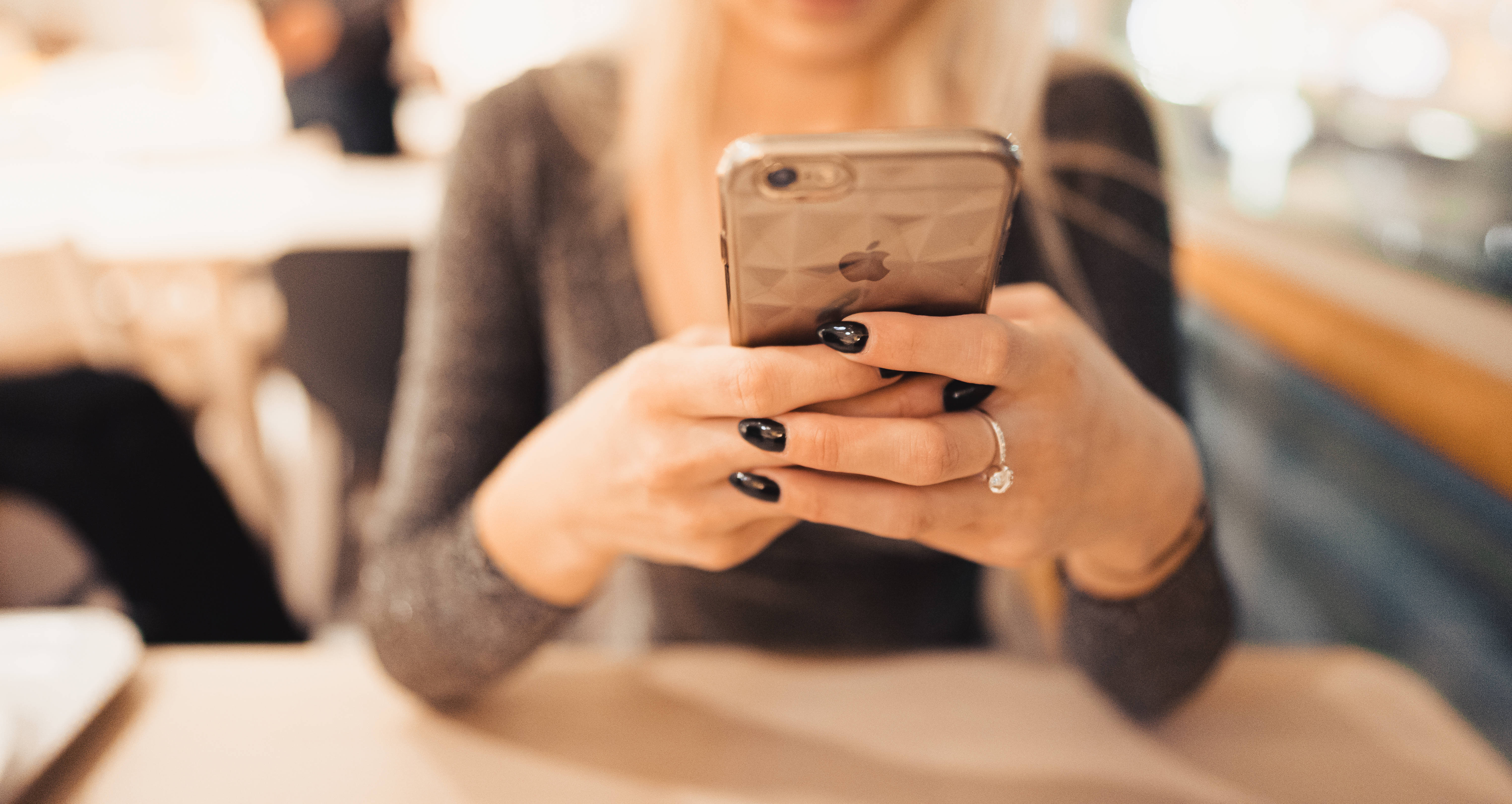 Valorant iPhone 壁紙 桌布 壁紙 — 一個塗黑色指甲油的人坐在室內手持智慧型手機的特寫。