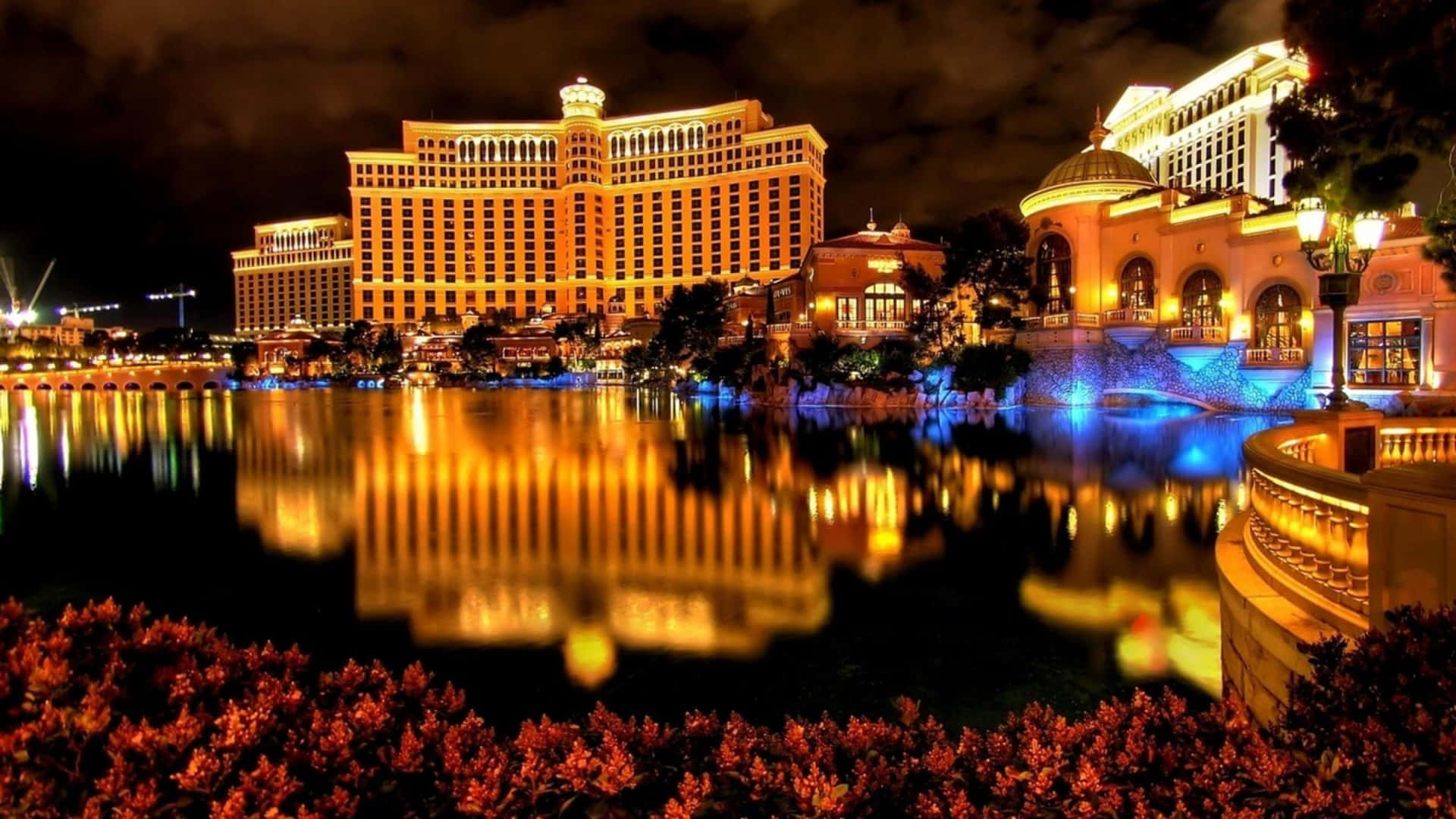 Casino 桌布 壁紙 — 一個壯麗的酒店綜合體夜景，倒映在平靜的水道上，鮮豔的橙色和藍色燈光點亮了整個場景。