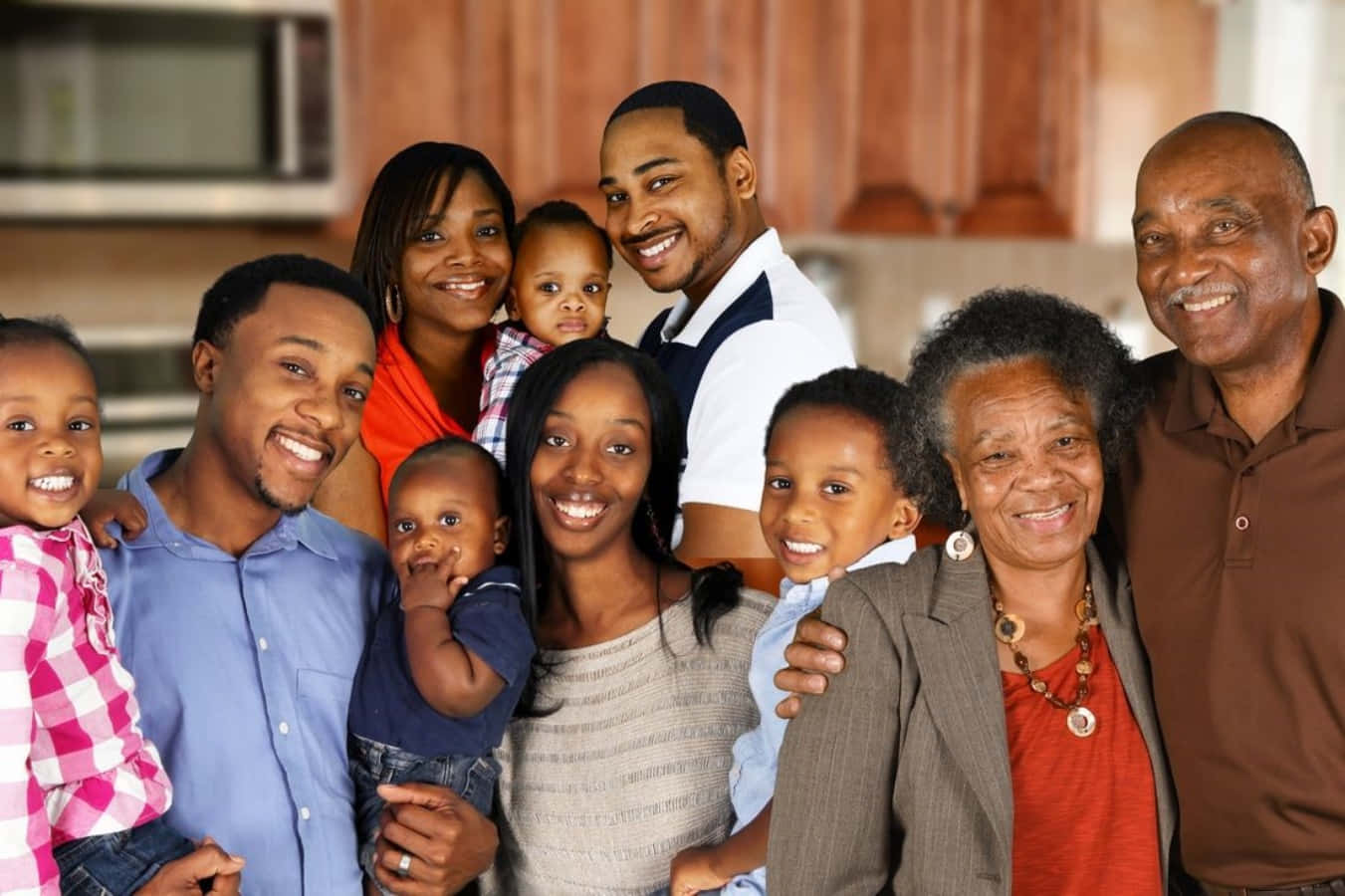 Black Family 桌布 壁紙 — 一個多代非裔美國家庭在明亮的廚房裡溫暖地微笑，廚房有木製櫥櫃和不鏽鋼電器。