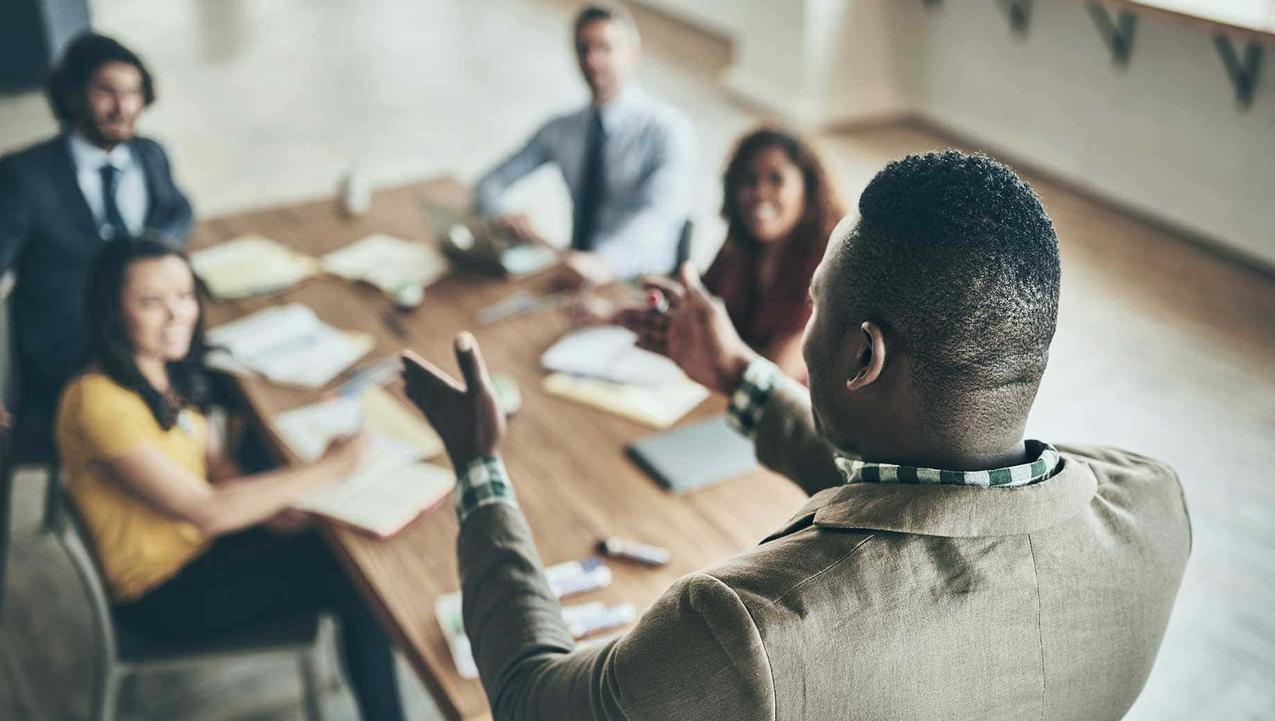 Leadership 桌布 壁紙 — 一個多元化的專業團隊圍繞著木製會議桌進行動態的腦力激盪會議。
